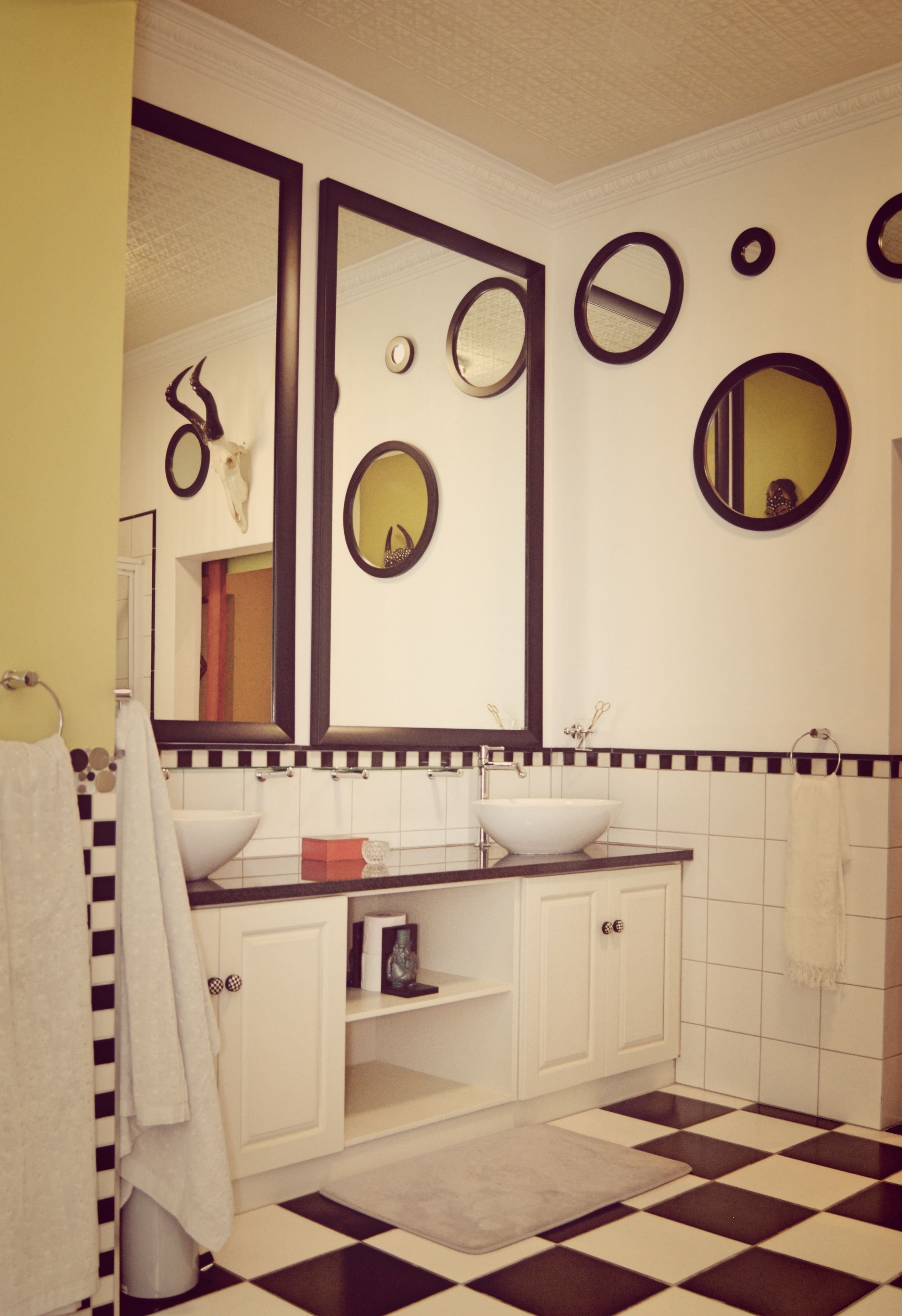 A bathroom with a checkered floor, white cabinets, a white sink, and multiple mirrors.