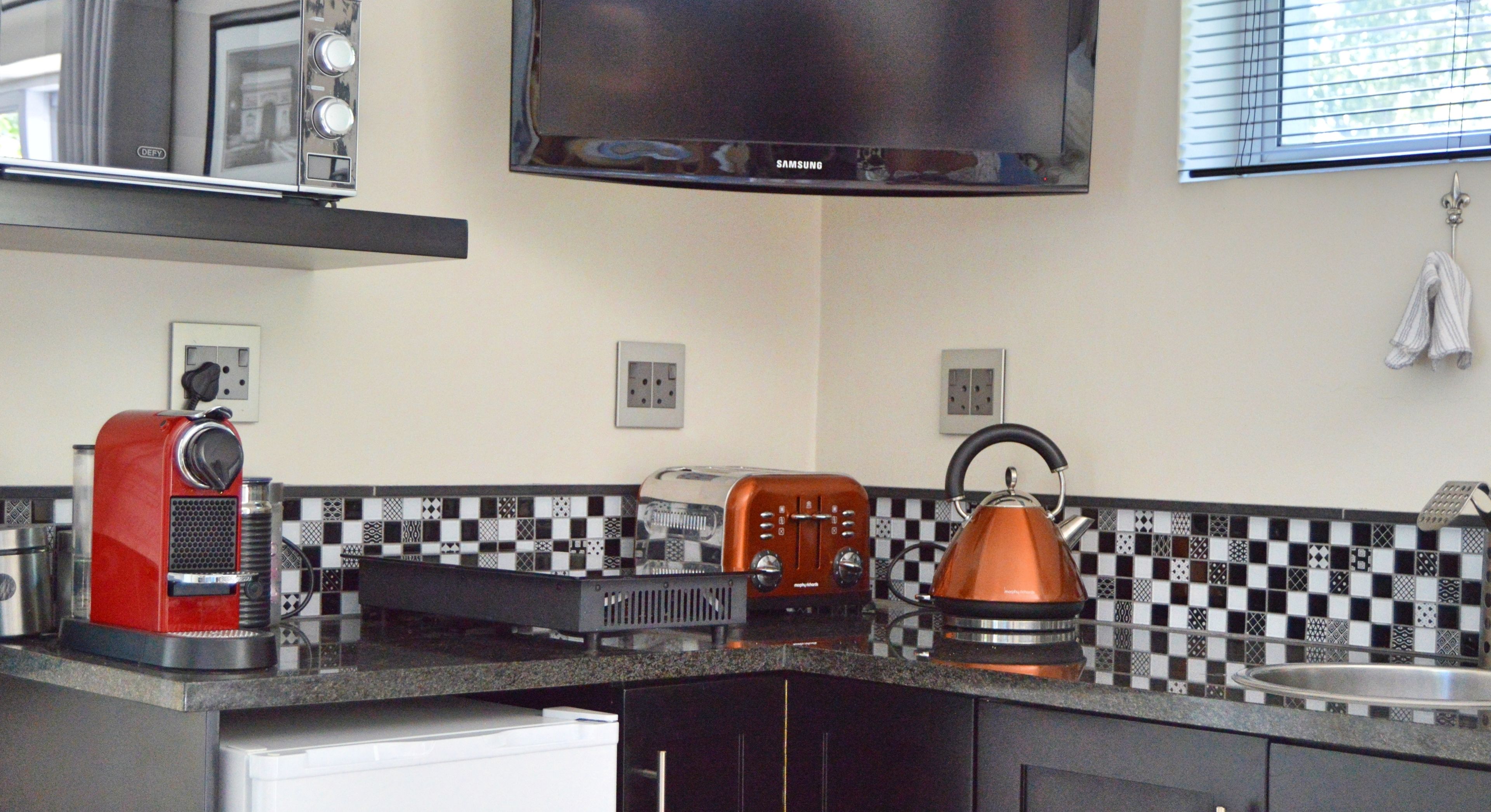Una cocina con microondas, tostadora, hervidor y televisor montado sobre la encimera.