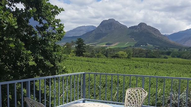 A deck with two chairs and a table, overlooking a vineyard and mountains. - 1AA Wilhelminia Apartments (Franschhoek)