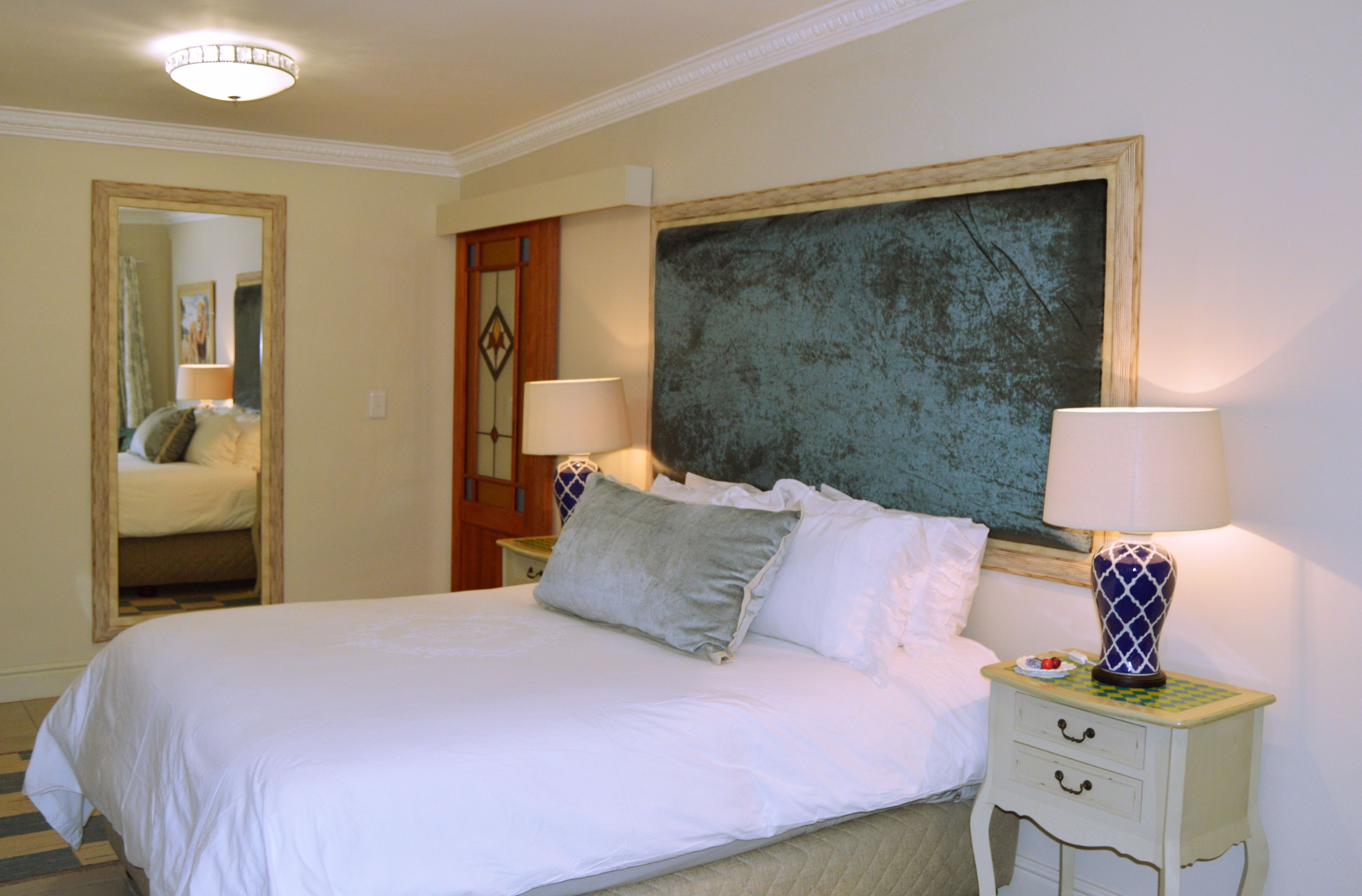 A neatly made bed with white linens and pillows, a bedside table with a lamp, and a large abstract painting on the wall.