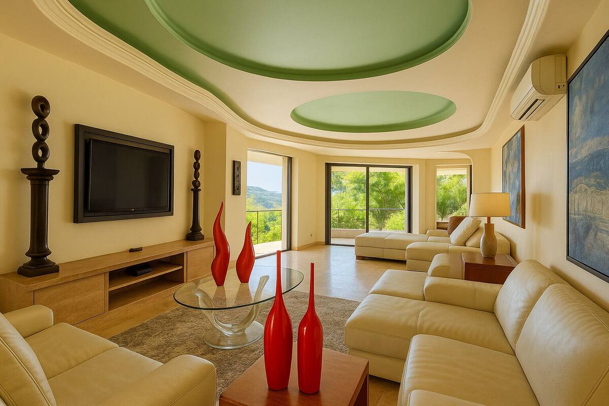 A spacious living room with a large flat-screen TV, beige sofas, a glass coffee table, and red vases.