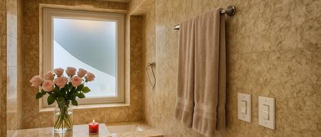 Une salle de bain avec un mur en marbre, une fenêtre, un porte-serviettes et un vase rempli de fleurs.