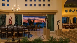 A spacious lobby with a view of the sunset over the ocean, a chandelier, and modern art sculptures. - Villa Armonia Luxury Suites (Puerto Vallarta)
