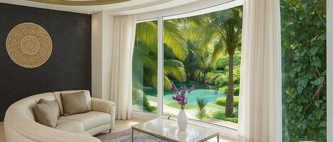 A spacious living room with a curved sofa, a coffee table, and a view of a lush garden through large windows.
