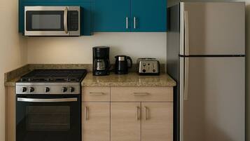 A modern kitchen with teal cabinets, a stainless steel microwave, a gas stove, a coffee maker, a toaster, and a refrigerator.