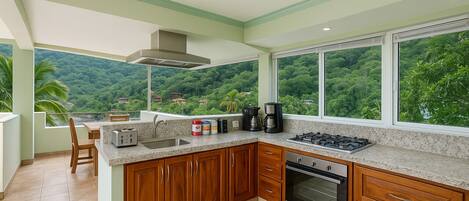 A kitchen with wooden cabinets, a granite countertop, and a view of lush greenery.