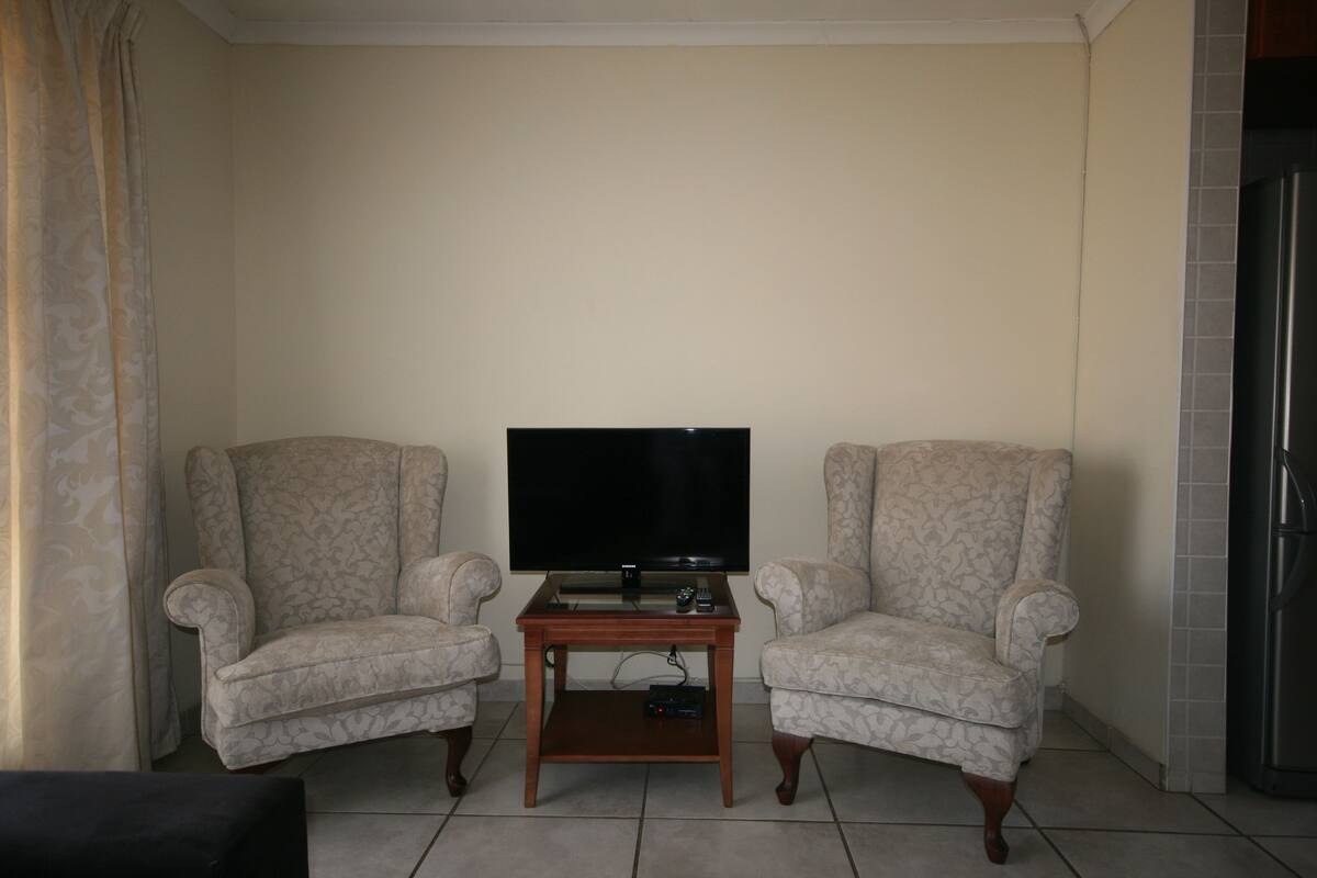 A living room with two patterned armchairs, a wooden coffee table, and a flat-screen TV.