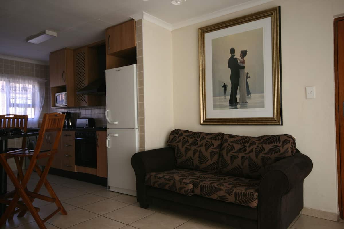A living room with a sofa, a dining table with chairs, a kitchen area with cabinets and appliances, and a framed picture on the wall.