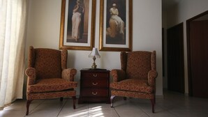 Een kamer met twee gestreepten fauteuils, een klein houten bijzettafeltje met een lamp en twee ingelijste schilderijen aan de muur.