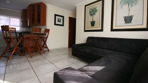 Een woonkamer met een zwarte bank, houten stoelen, een eettafel en ingelijste foto's aan de muur.