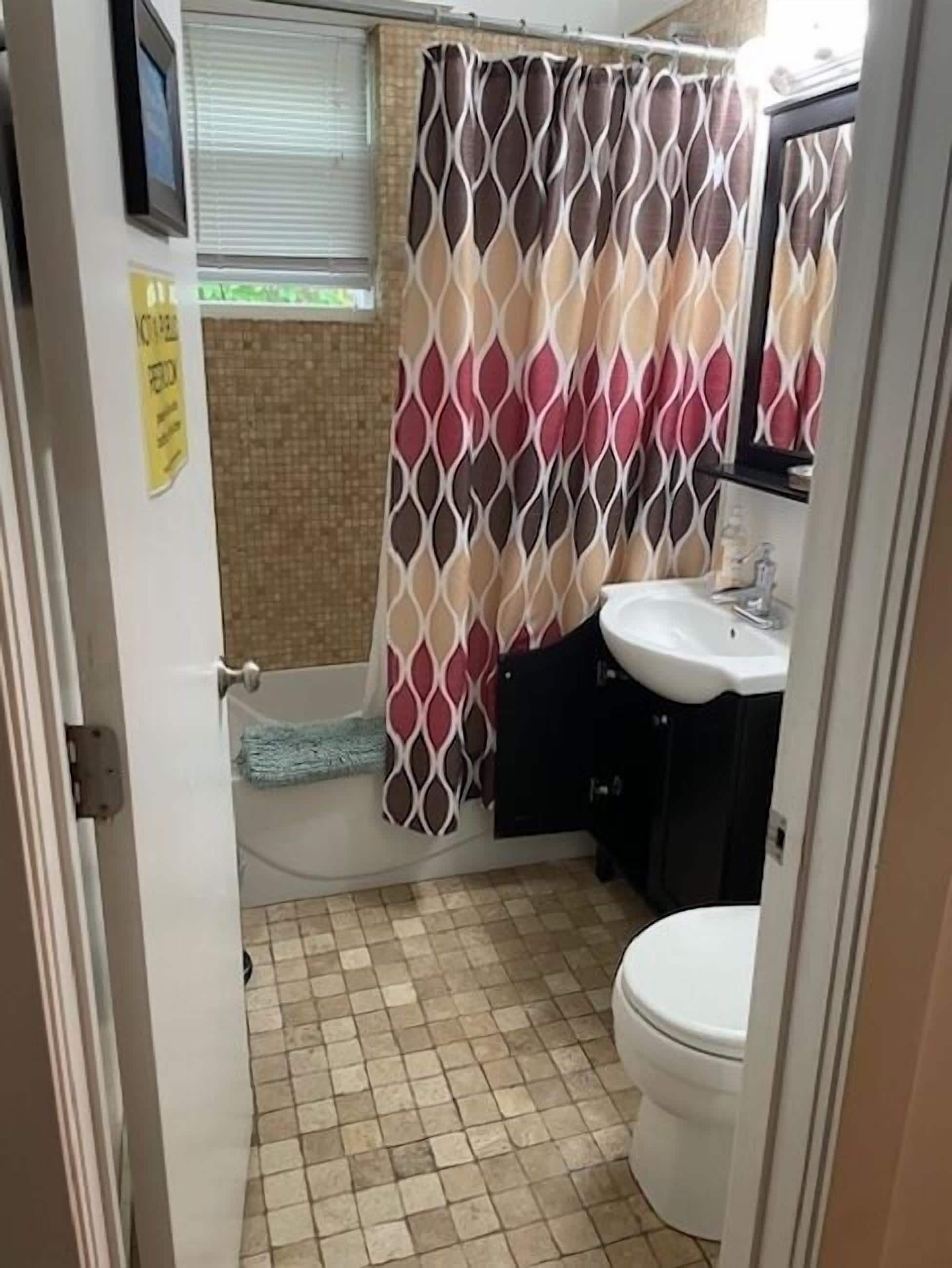 Une salle de bain avec un sol carrelé, un lavabo blanc, des toilettes et un rideau de douche à motifs géométriques.