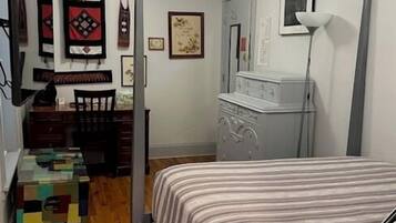 A bedroom with a bed, a dresser, a desk, and a chair. There are wall decorations and a ceiling fan.