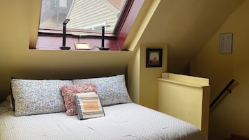 A bedroom with a skylight, a bed with floral bedding, a welcome sign, a framed picture, and a staircase.