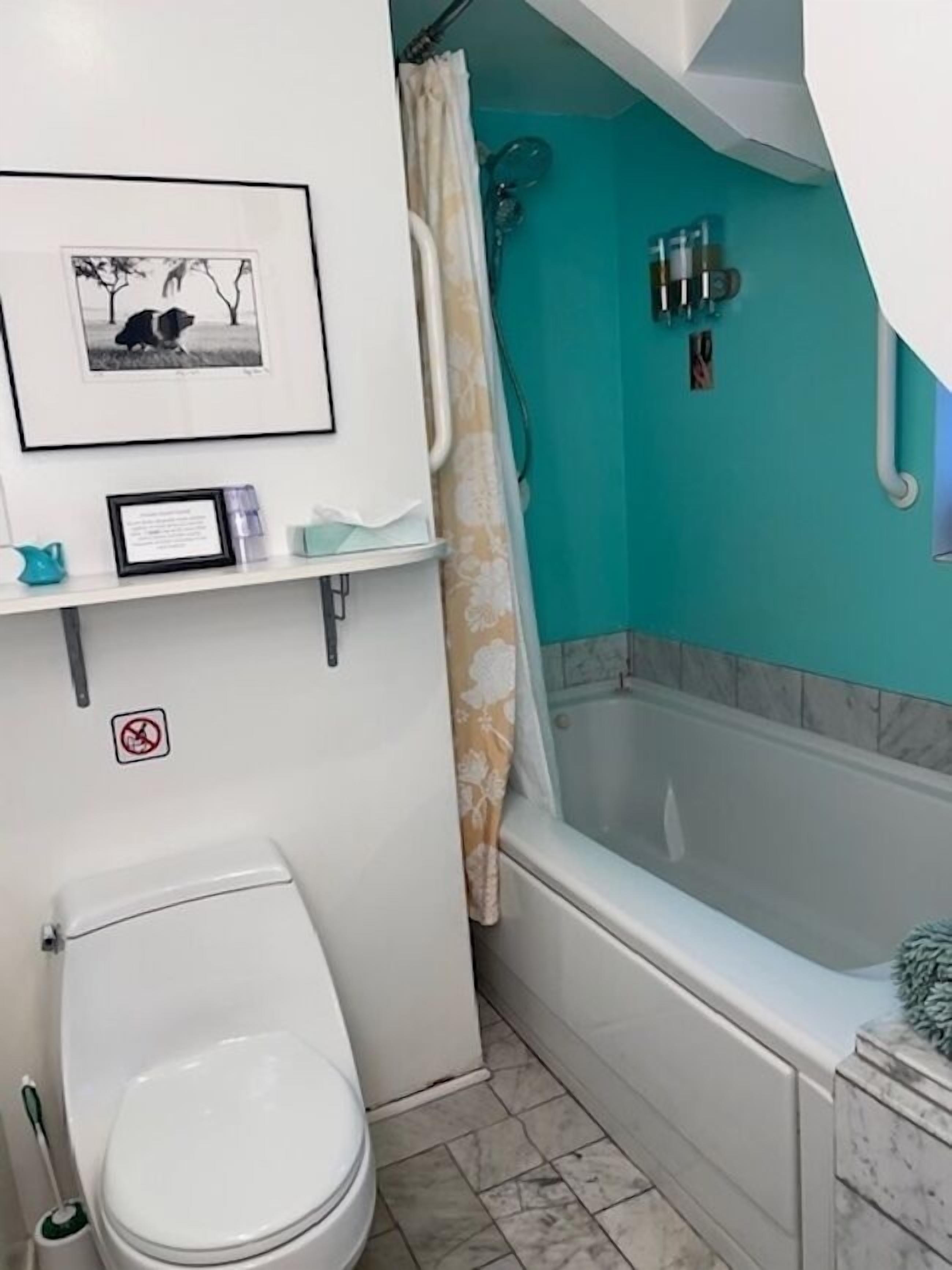 A bathroom with a toilet, a bathtub, a shower curtain, and a framed picture on the wall.