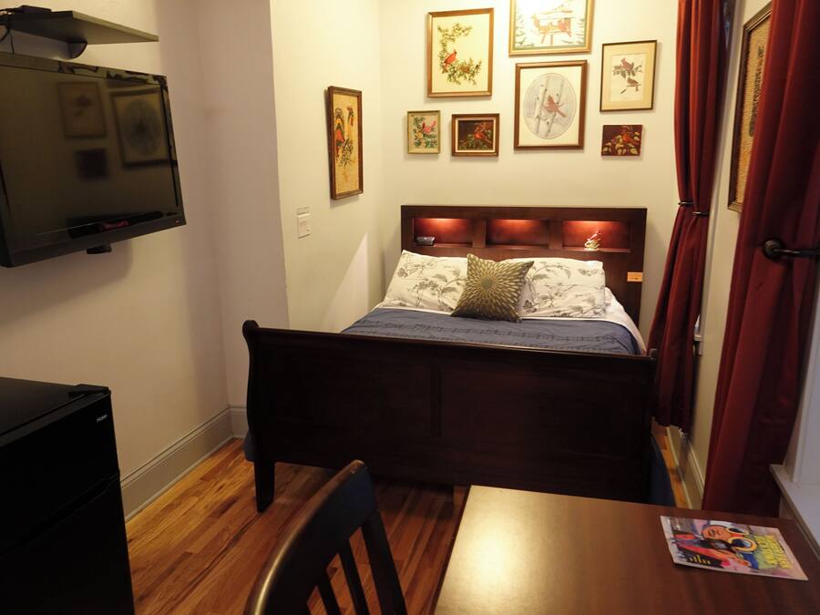 Ein Schlafzimmer mit einem Bett, einem Schreibtisch, einem Fernseher und verschiedenen gerahmten Bildern an der Wand.