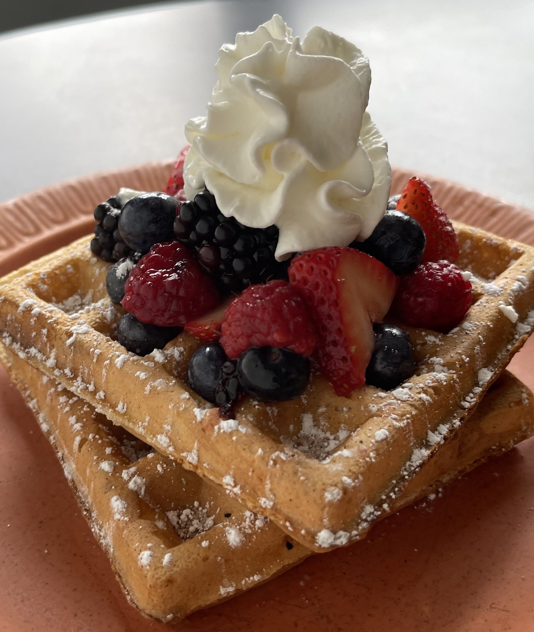 Una pila de gofres cubiertos de crema batida y frutos rojos frescos.