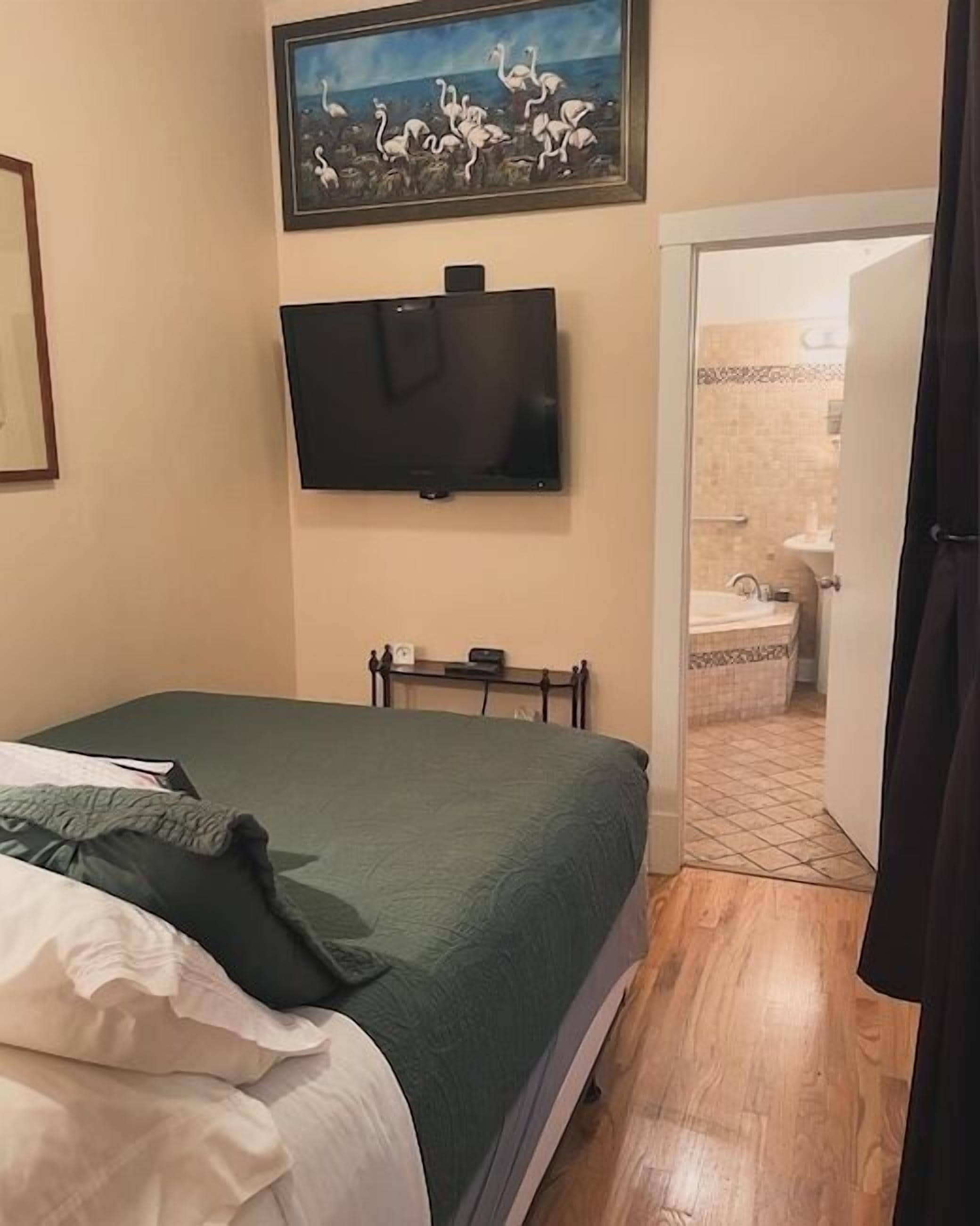 A bedroom with a bed, a television mounted on the wall, and a painting above the bed.