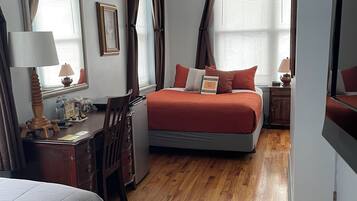 A bedroom with a bed, a desk, a chair, a dresser, a ceiling fan, and a window with curtains.