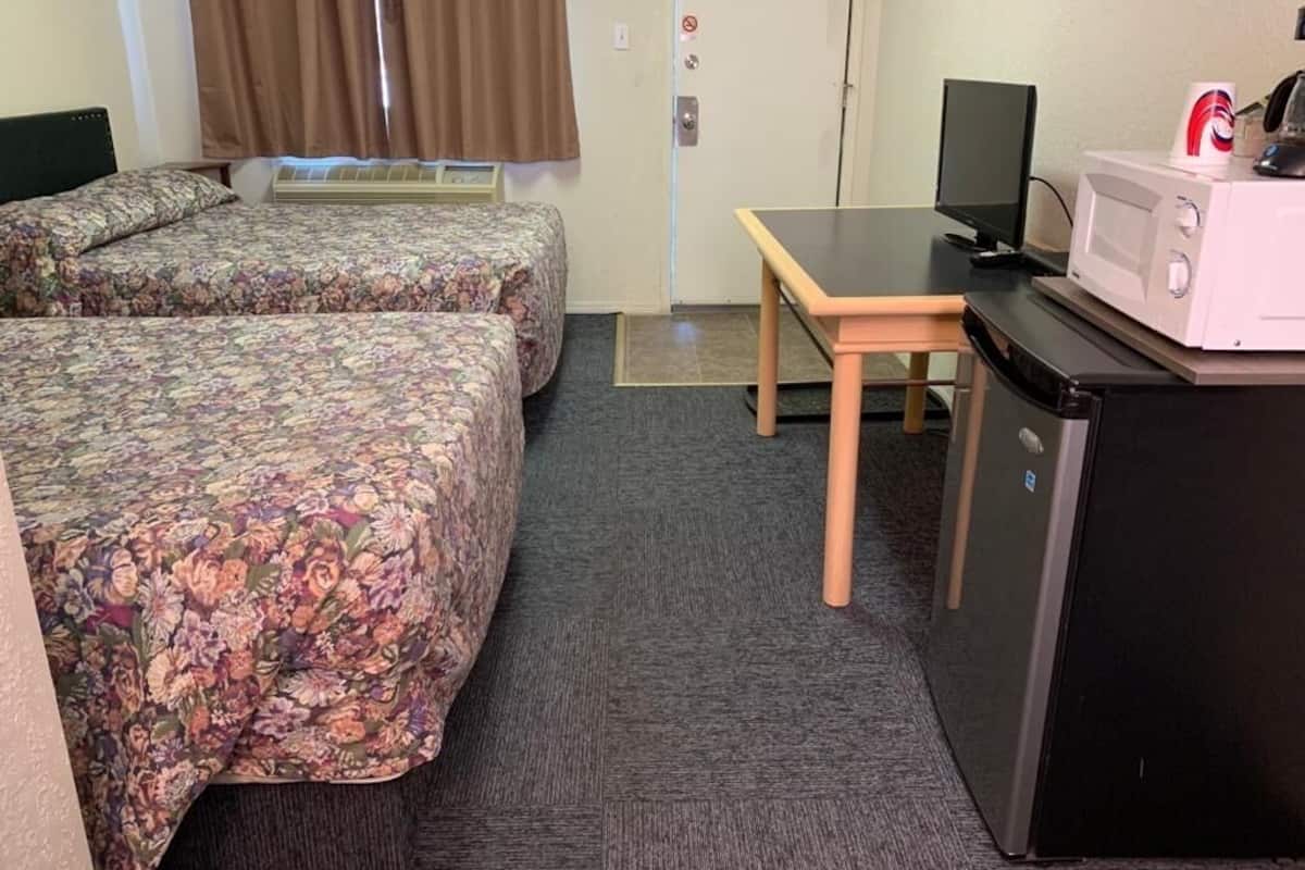 A hotel room with two beds, a desk, a microwave, and a television.