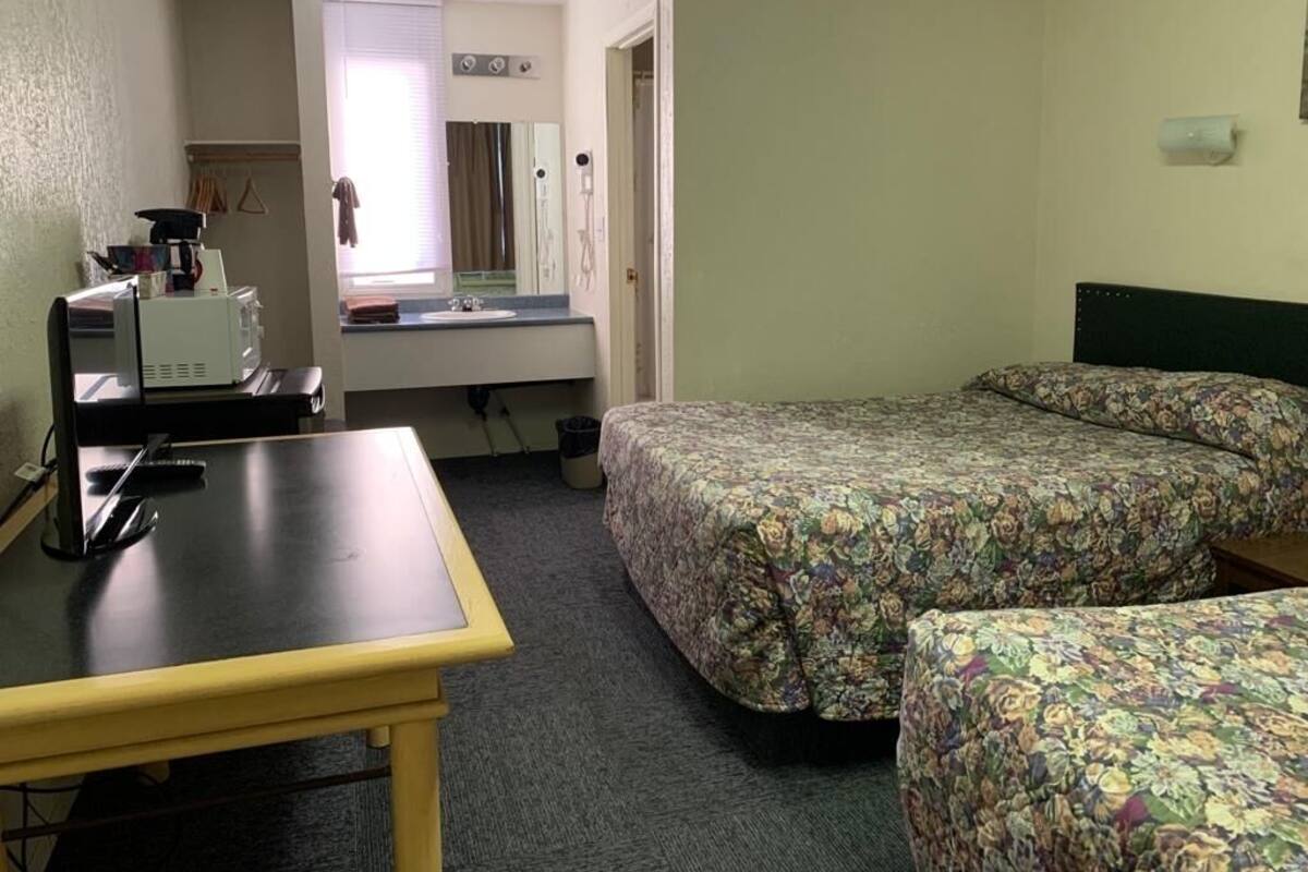 A hotel room with two beds, a desk, a chair, a small table, and a window with blinds.