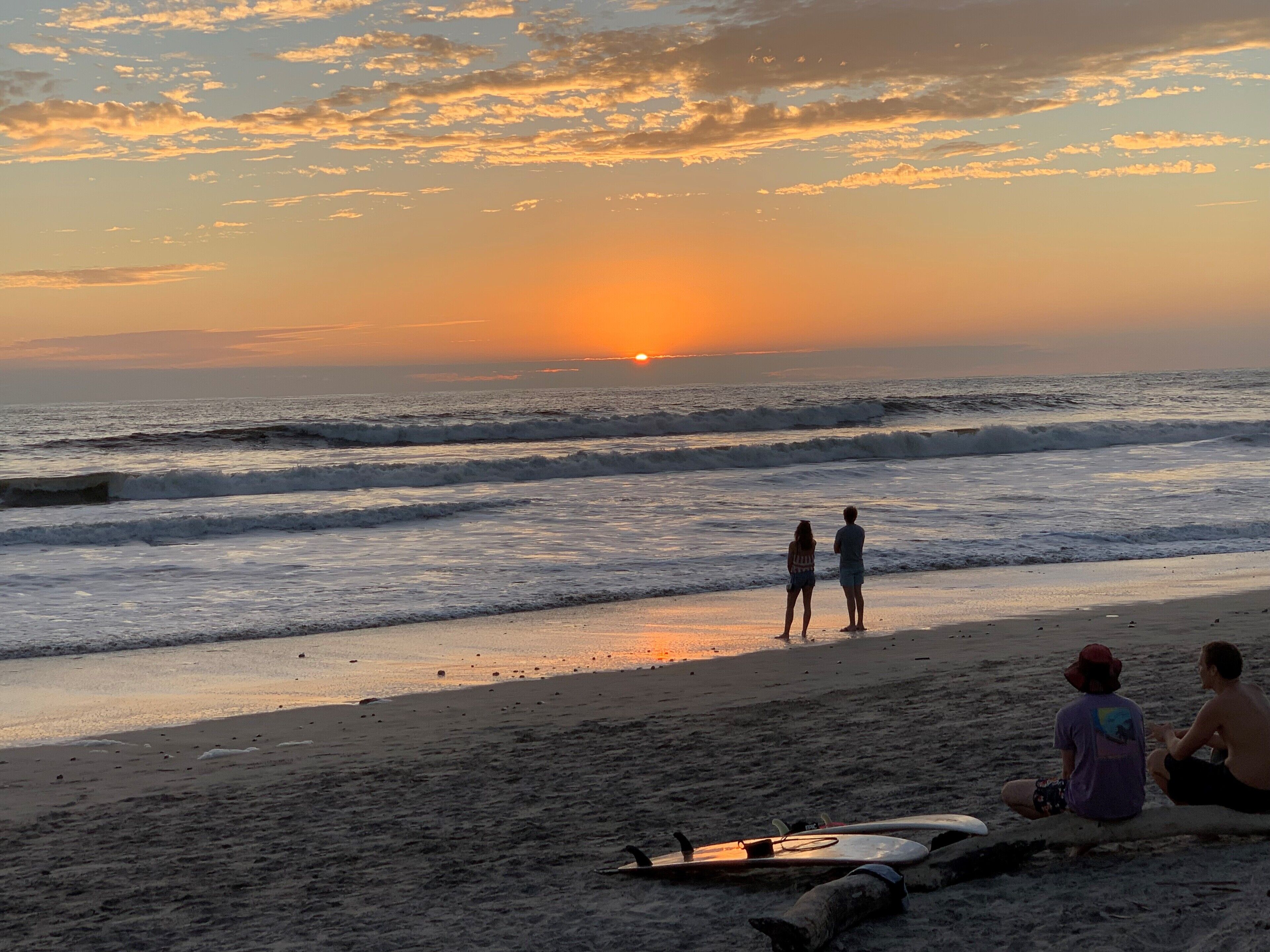 Ein Strand mit Wellen, einem Sonnenuntergang und Menschen.