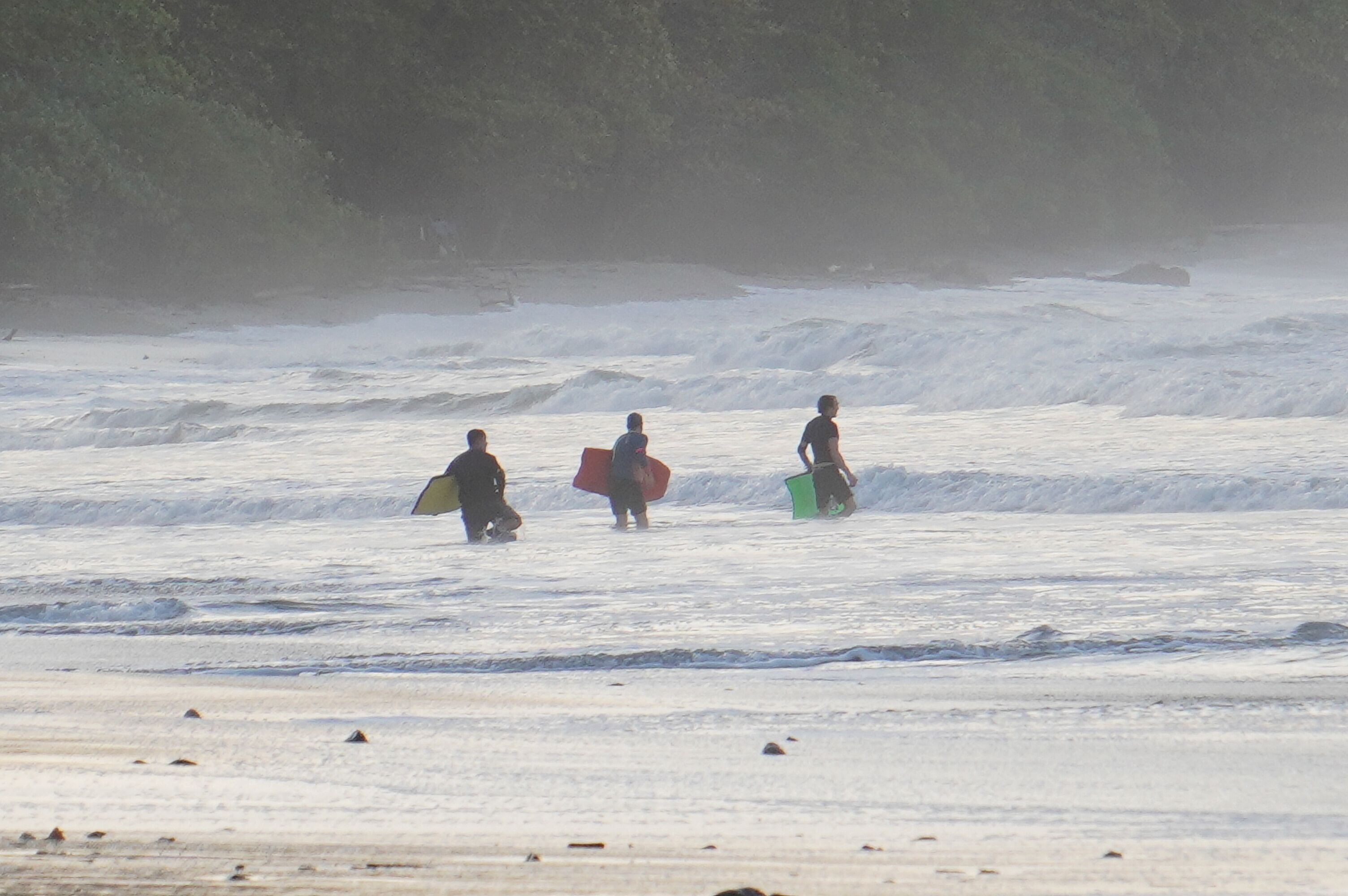 Drie mensen lopen over het strand met surfplanken.