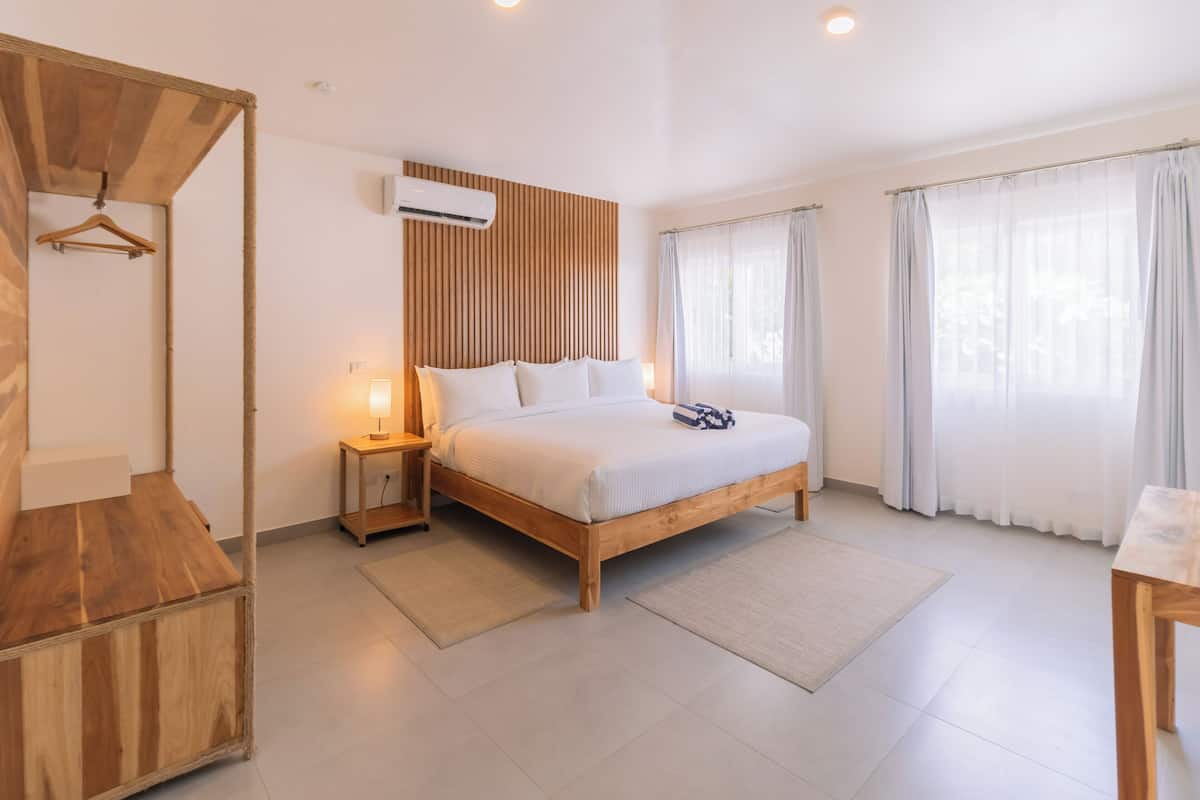 A modern bedroom with a wooden bed, bedside tables, a hanging wardrobe, and large windows with curtains.