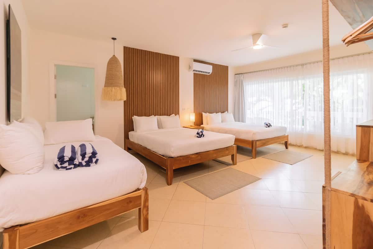 A hotel room with two wooden beds, a large mirror, a ceiling fan, and a window with sheer curtains.