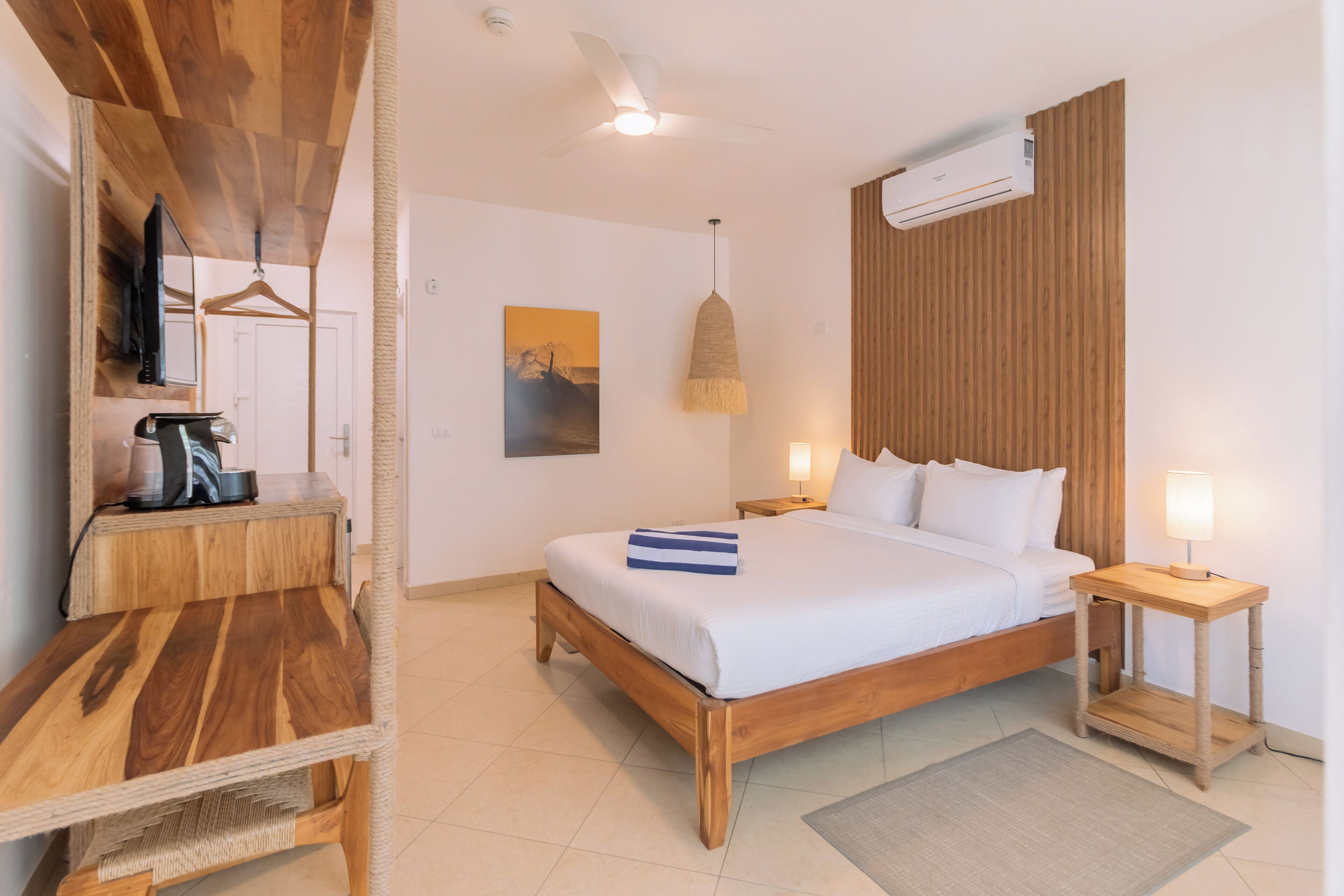 A hotel room with a wooden bed, a bedside table, a hanging light, and a wall-mounted air conditioner.