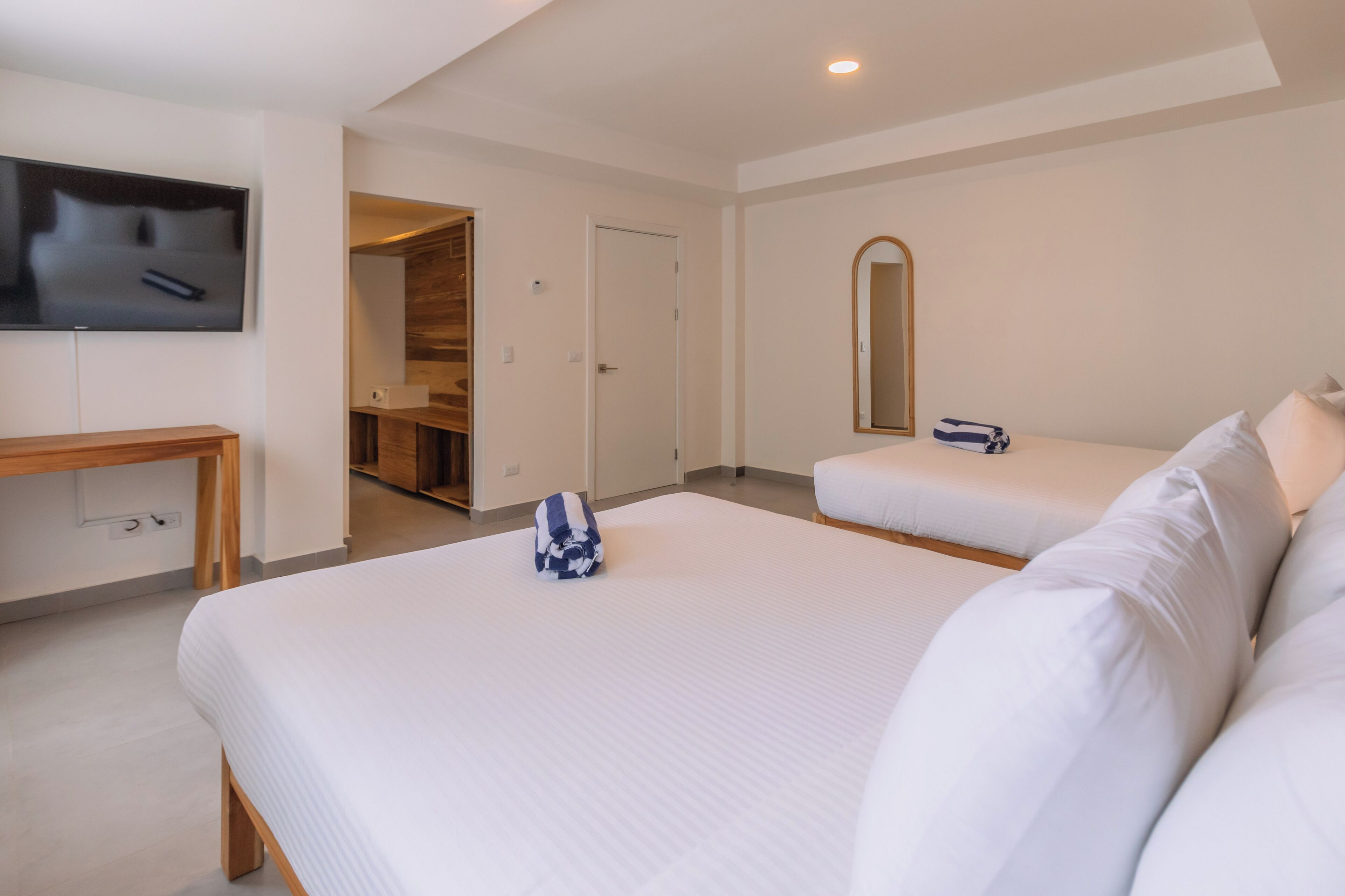 Habitación de hotel con dos camas, un televisor montado en la pared, un escritorio de madera y un espejo.