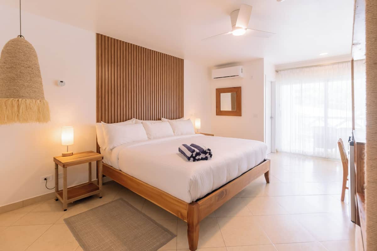 A bedroom with a wooden bed, bedside lamps, a ceiling fan, and a large window with sheer curtains.
