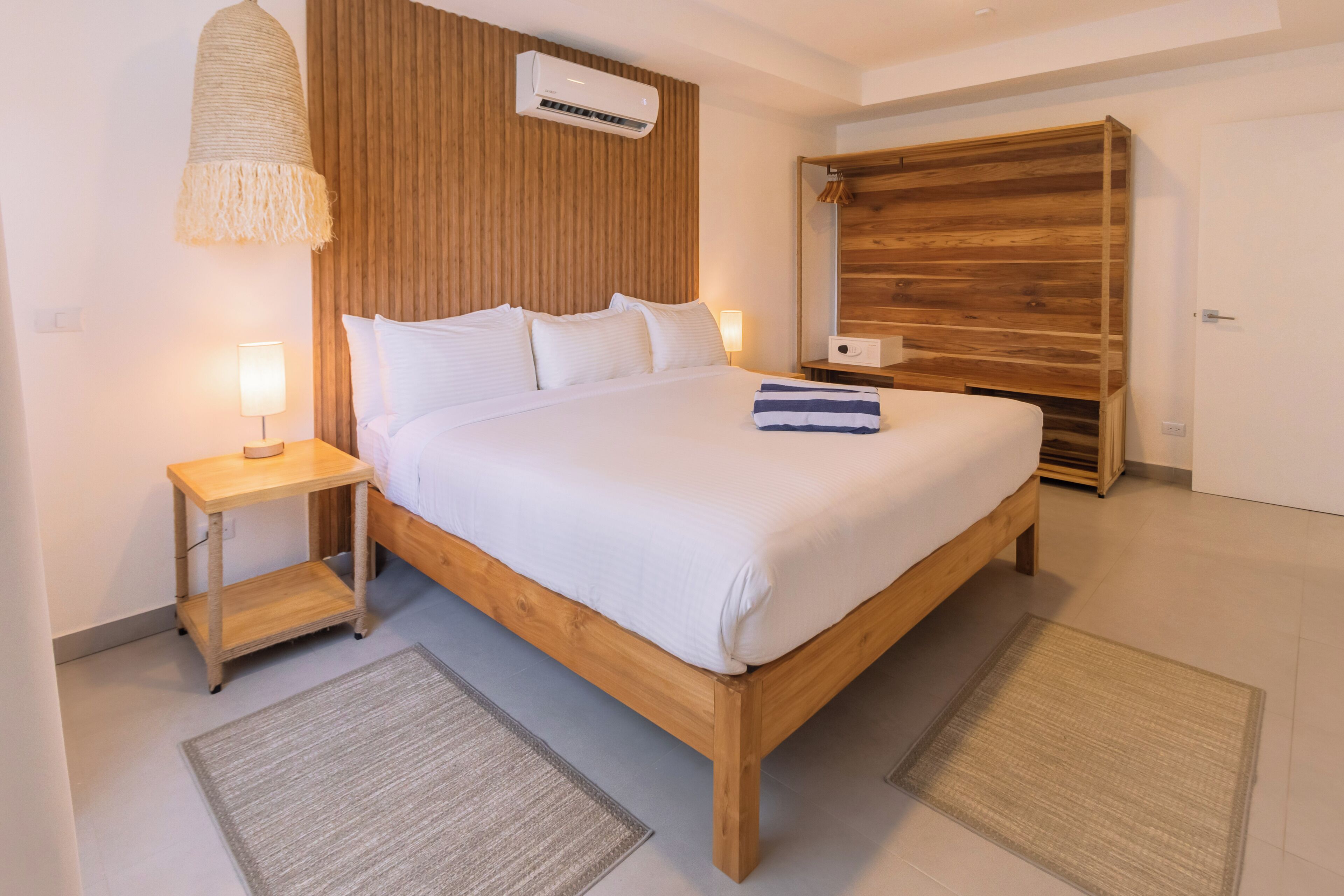 Un dormitorio con cabecera de cama de madera, ropa de cama blanca, una mesita de noche con lámpara y un armario de madera.