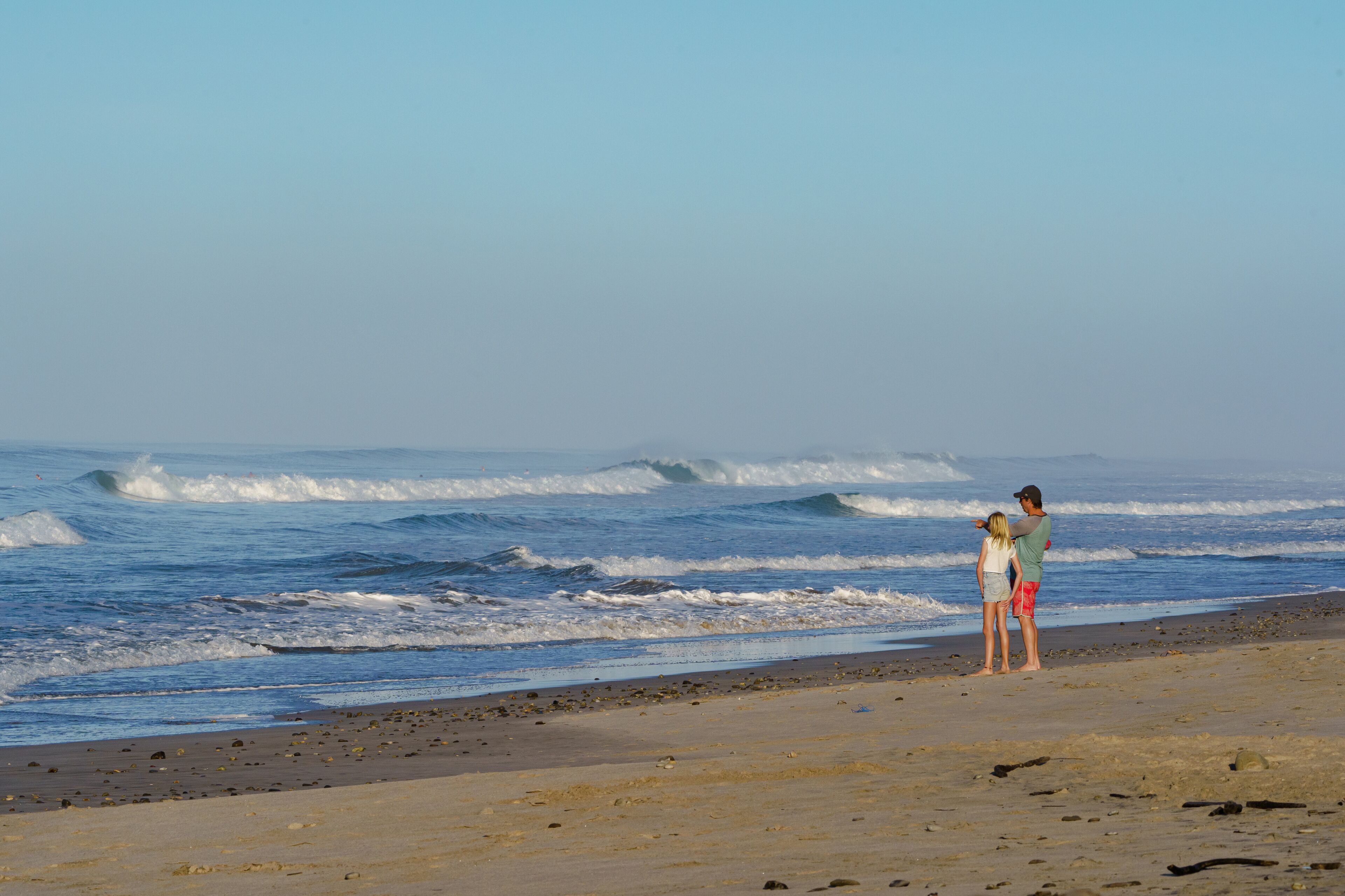 Ein Strand mit Wellen und zwei Personen am Ufer.