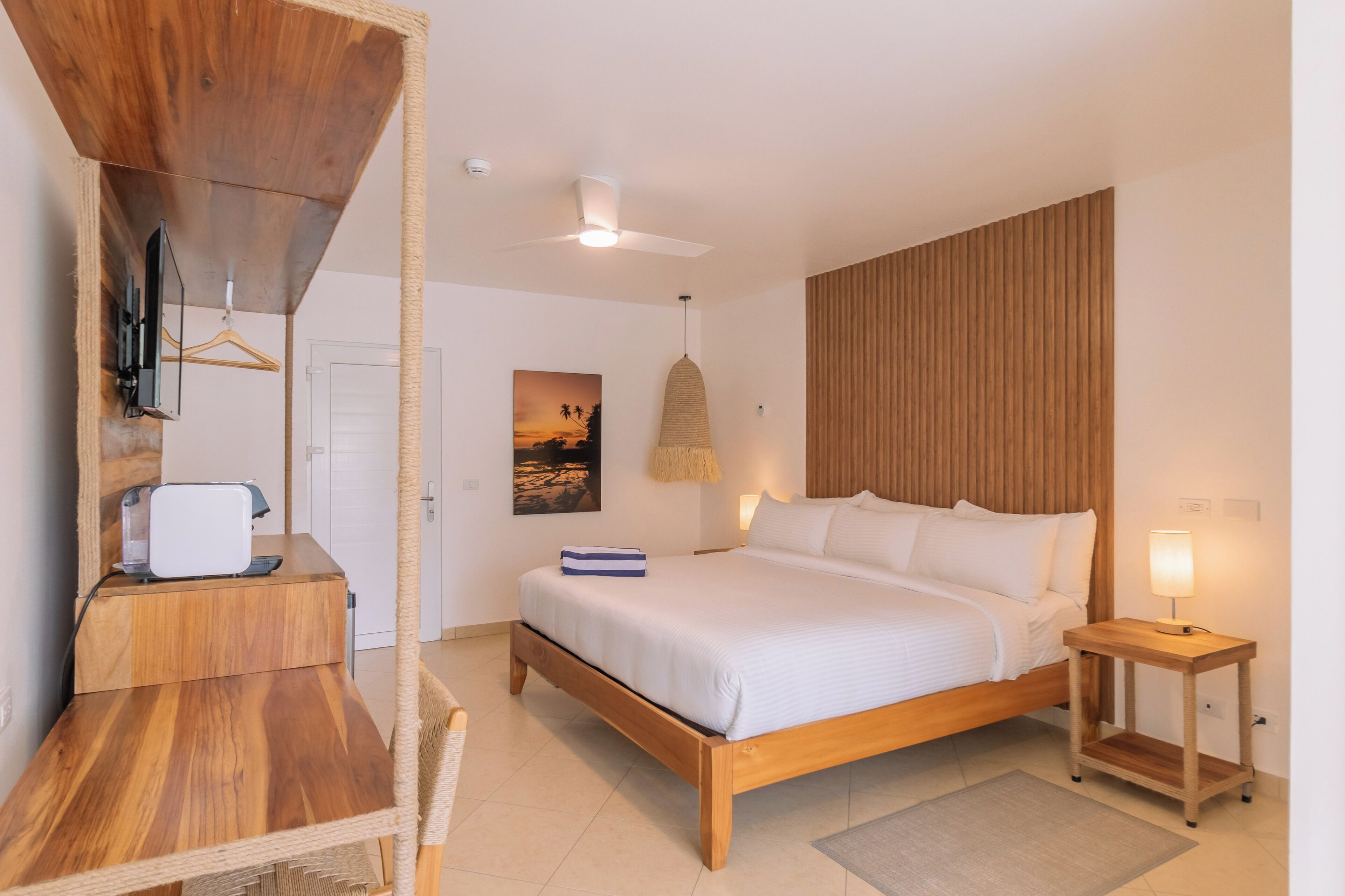 A bedroom with a wooden bed, bedside table, and a desk with a chair.