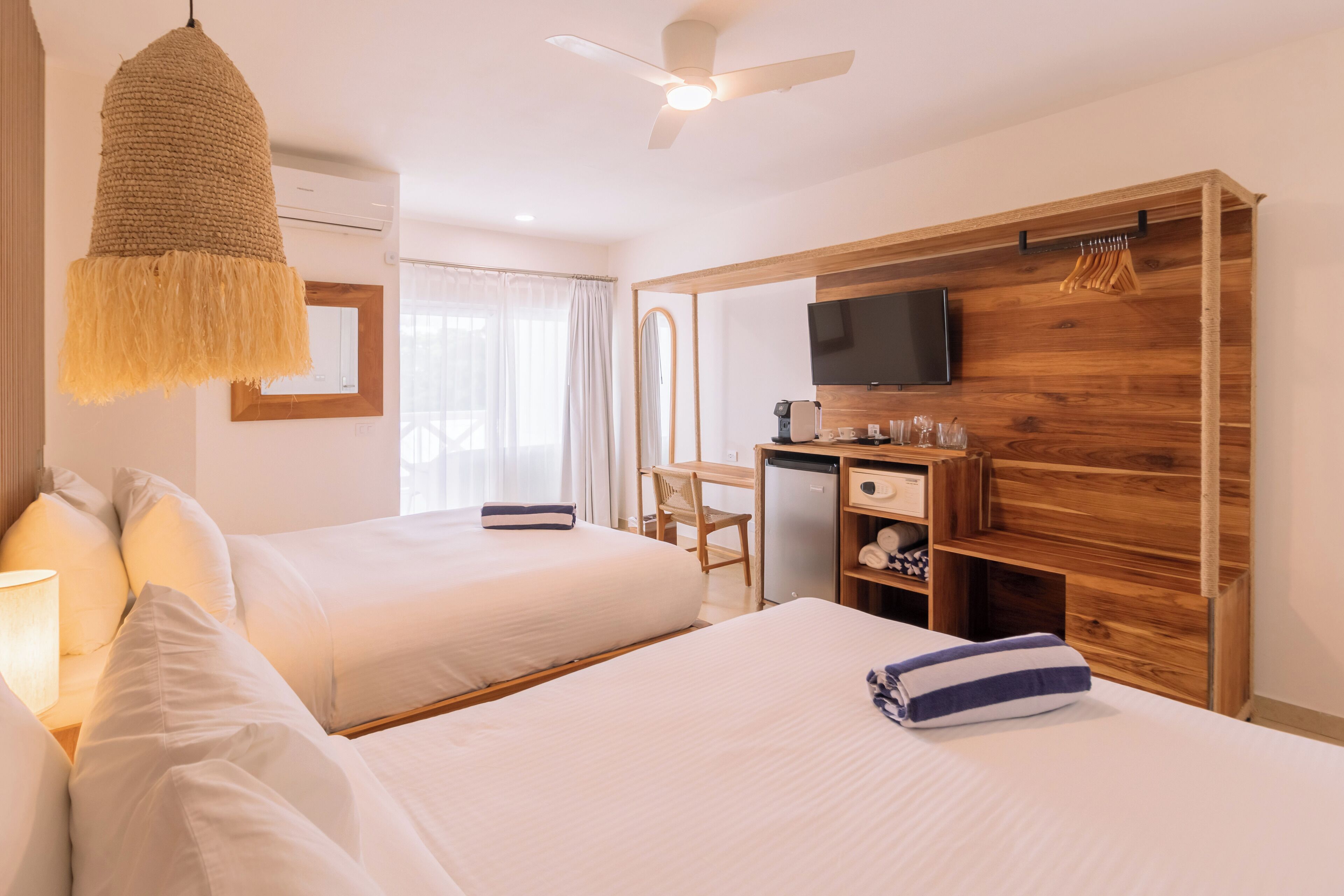 Hotellihuone, jossa on kaksi sänkyä, työpöytä, jossa on televisio, kattotuuletin ja puinen vaatekaappi.