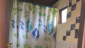 Een kleine badkamer met toilet, wastafel en douchegordijn met een groen en blauw patroon.