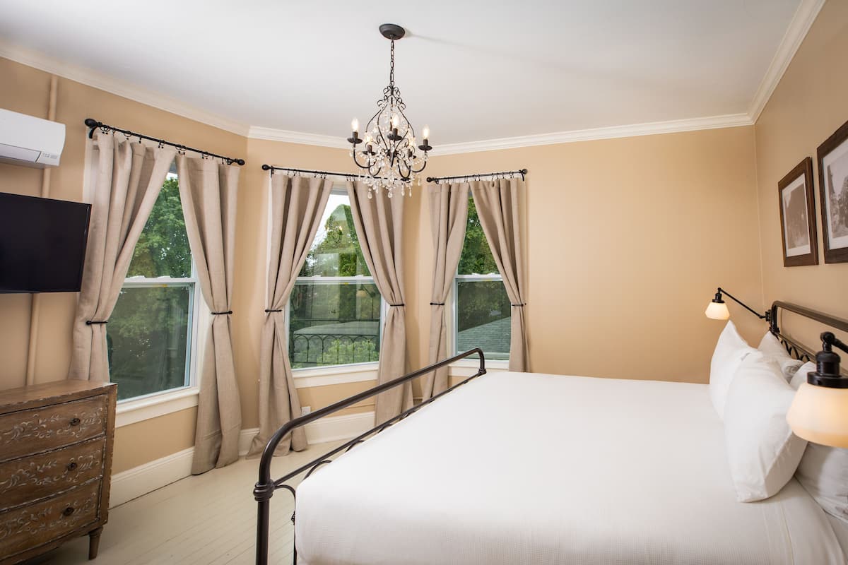 Une chambre à coucher avec un lit, une commode, un lustre et une fenêtre avec des rideaux.