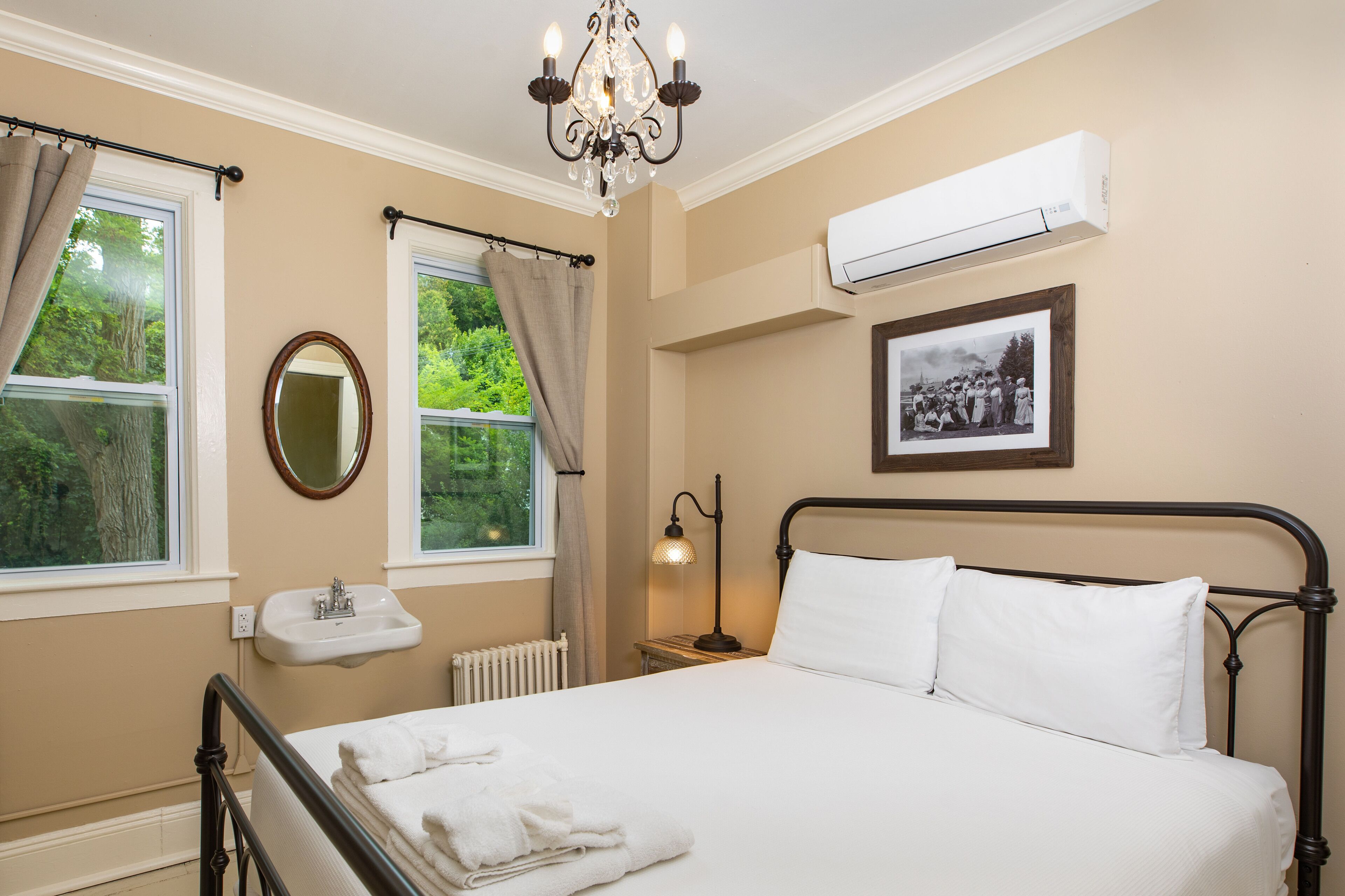 Une chambre à coucher comprenant un lit, une lampe de chevet, une fenêtre avec des rideaux, un climatiseur fixé au mur et un tableau encadré.