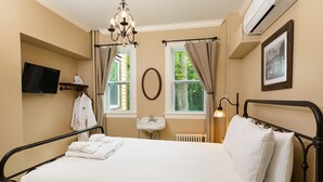 A bedroom with a bed, a TV, a sink, and a window with curtains.