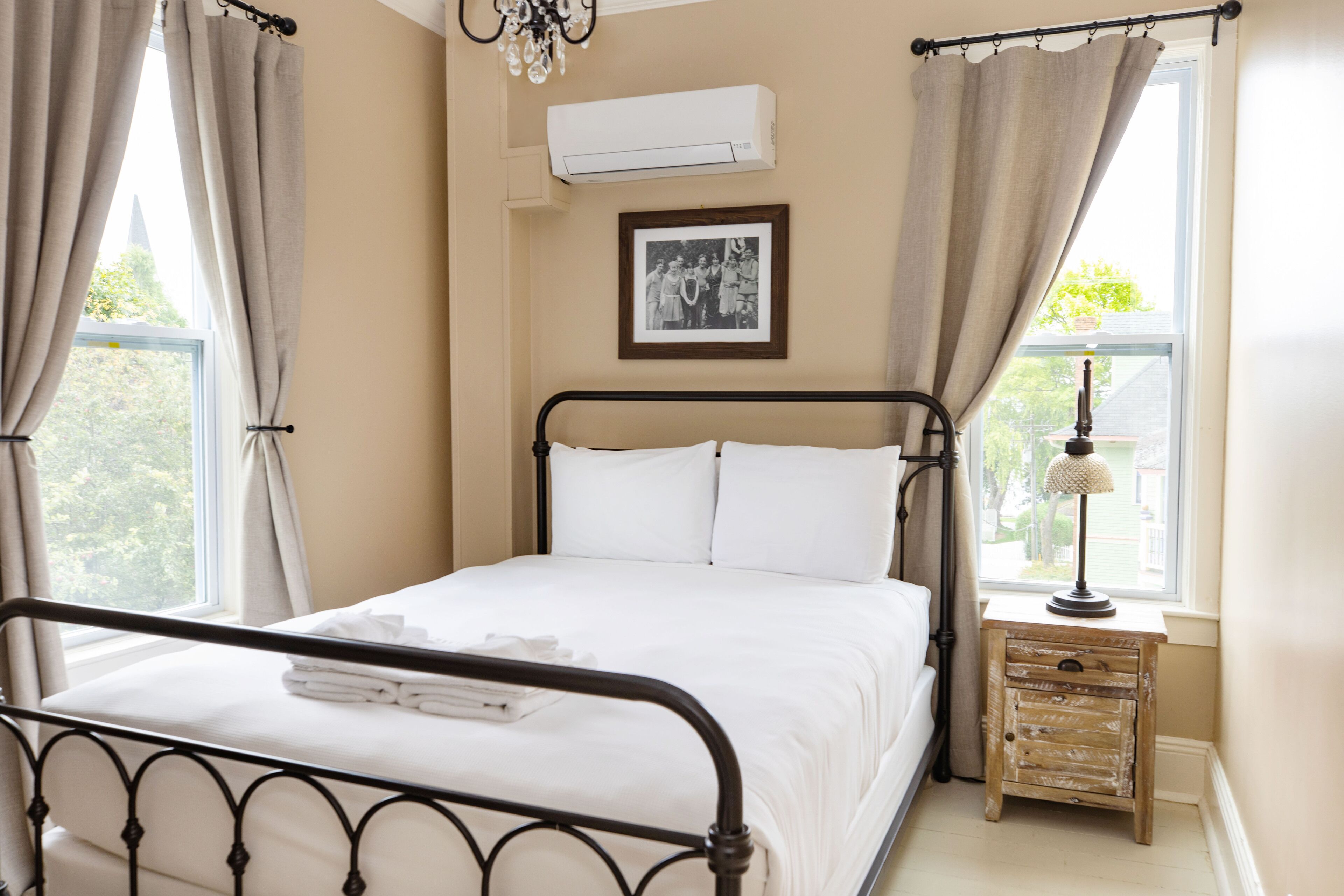 A neatly made bed with white linens, a small bedside table with a lamp, and a framed photo on the wall.