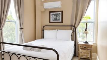 A neatly made bed with white linens, a small bedside table with a lamp, and a framed photo on the wall.
