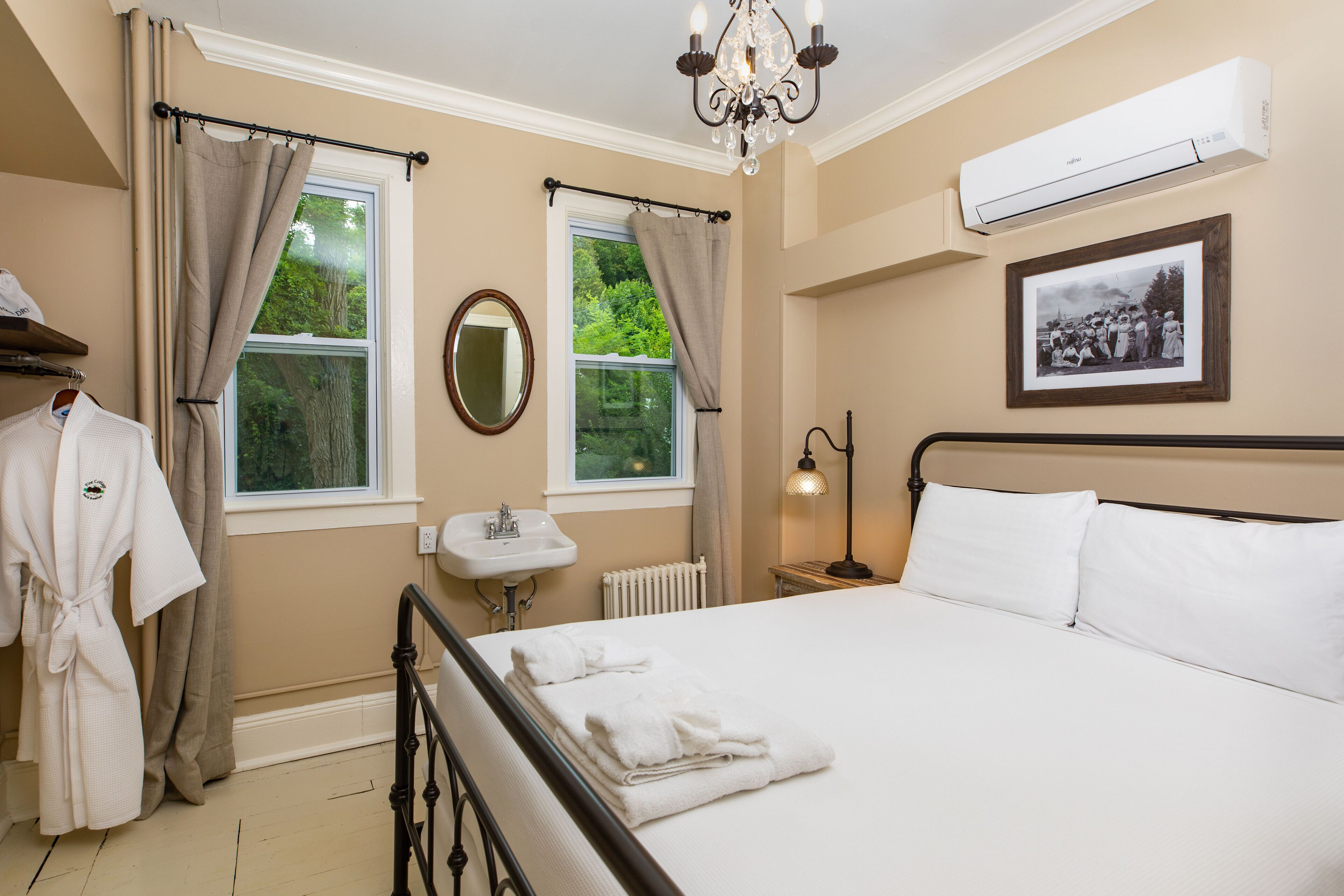 A bedroom with a bed, a nightstand, a mirror, a window with curtains, a radiator, and an air conditioning unit.