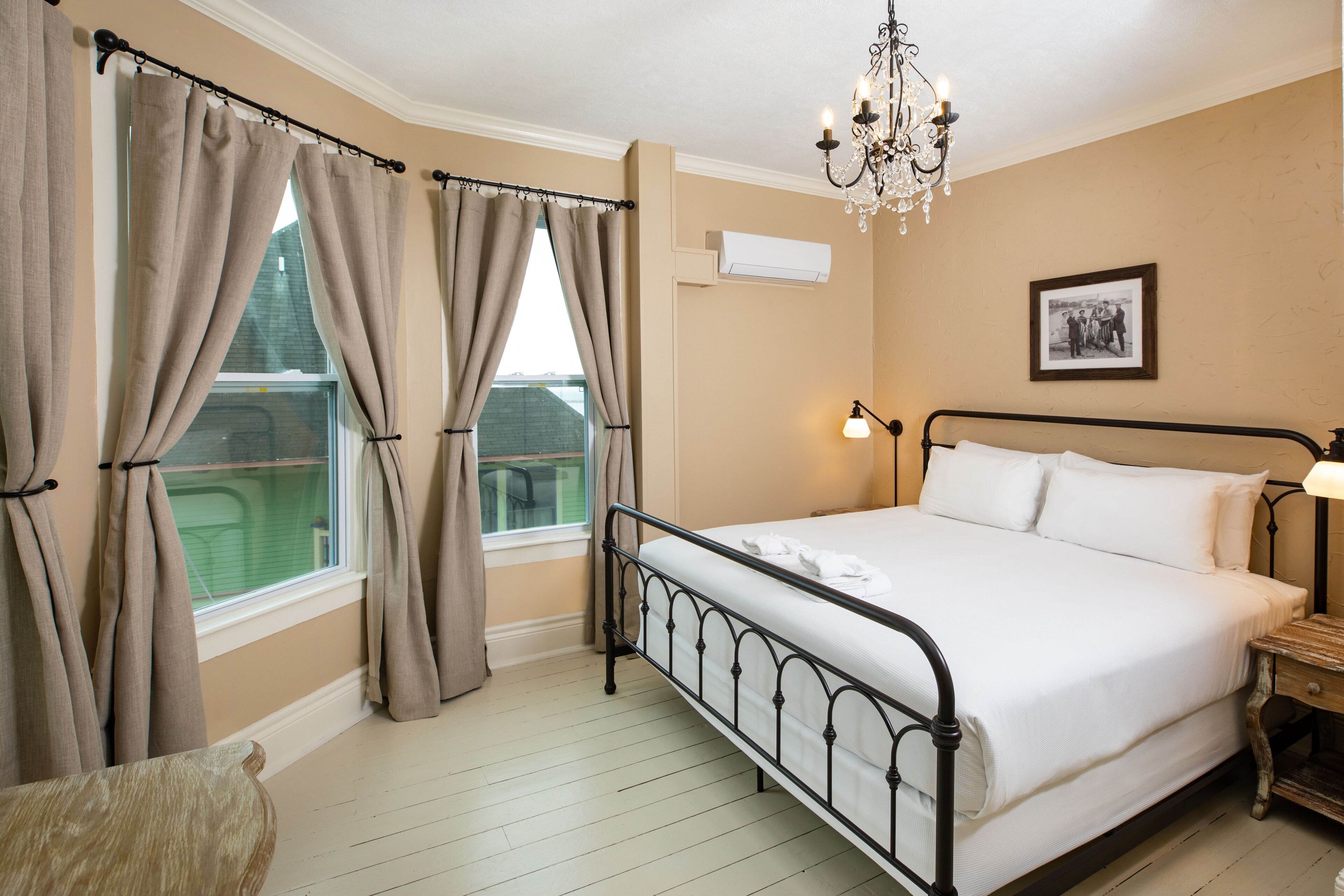 Une chambre à coucher avec un lit, des rideaux, un lustre, une table de chevet et un tableau au mur.