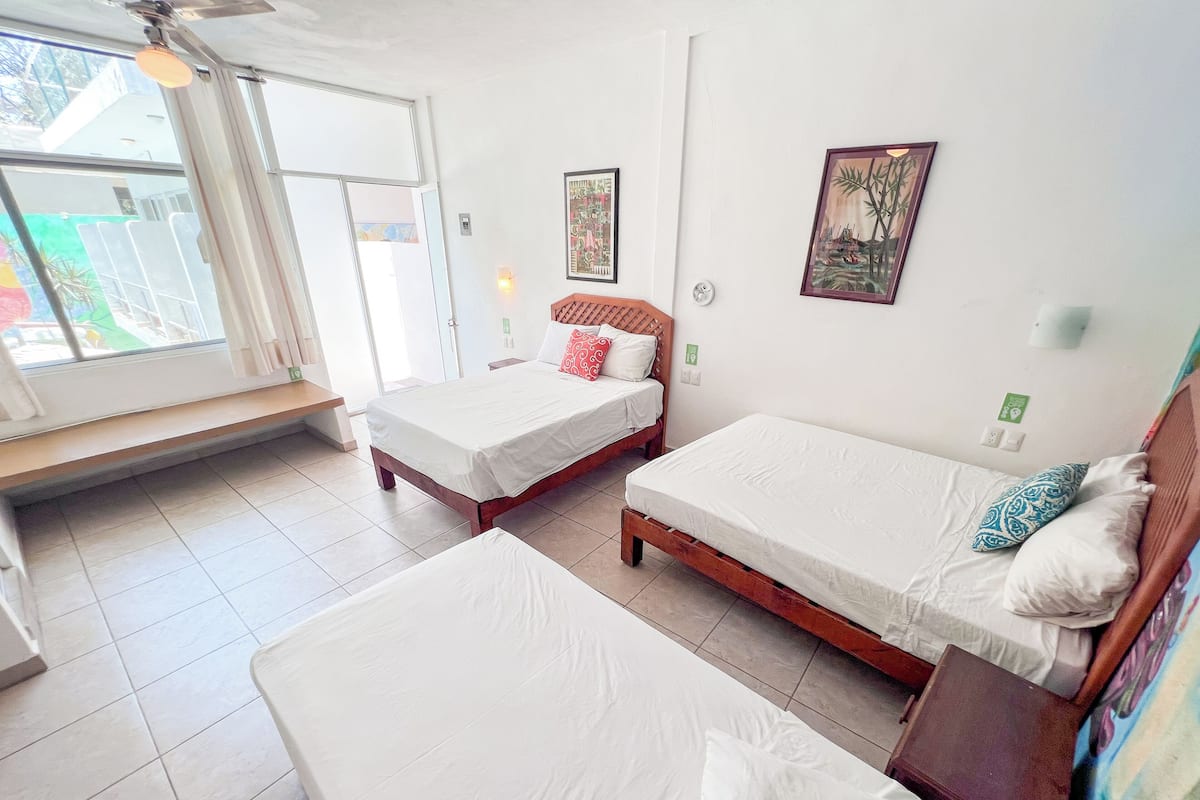 A hotel room with two single beds, a bench, a window with a view, and a wall-mounted light.