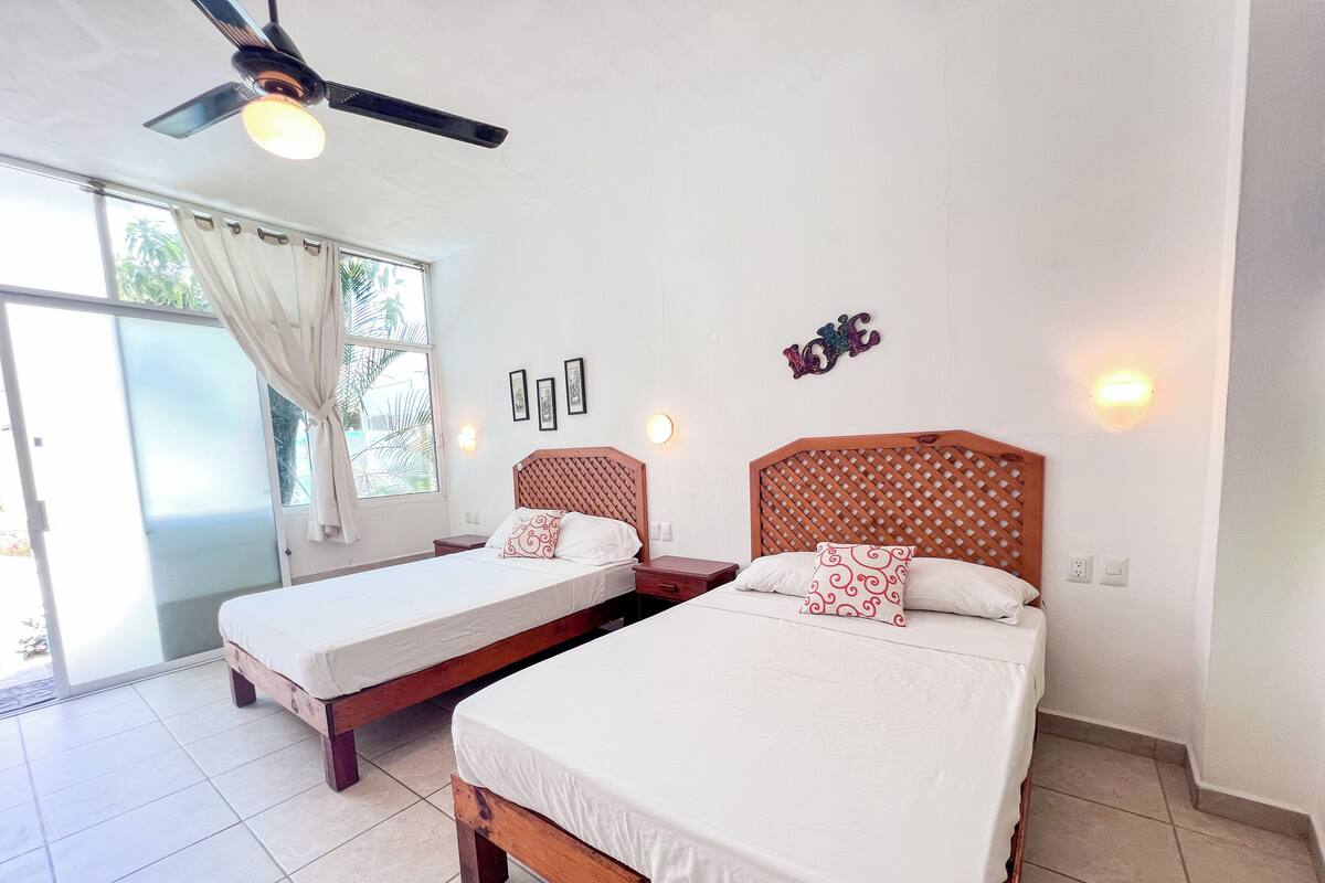A hotel room with two beds, a ceiling fan, and a large window with curtains.
