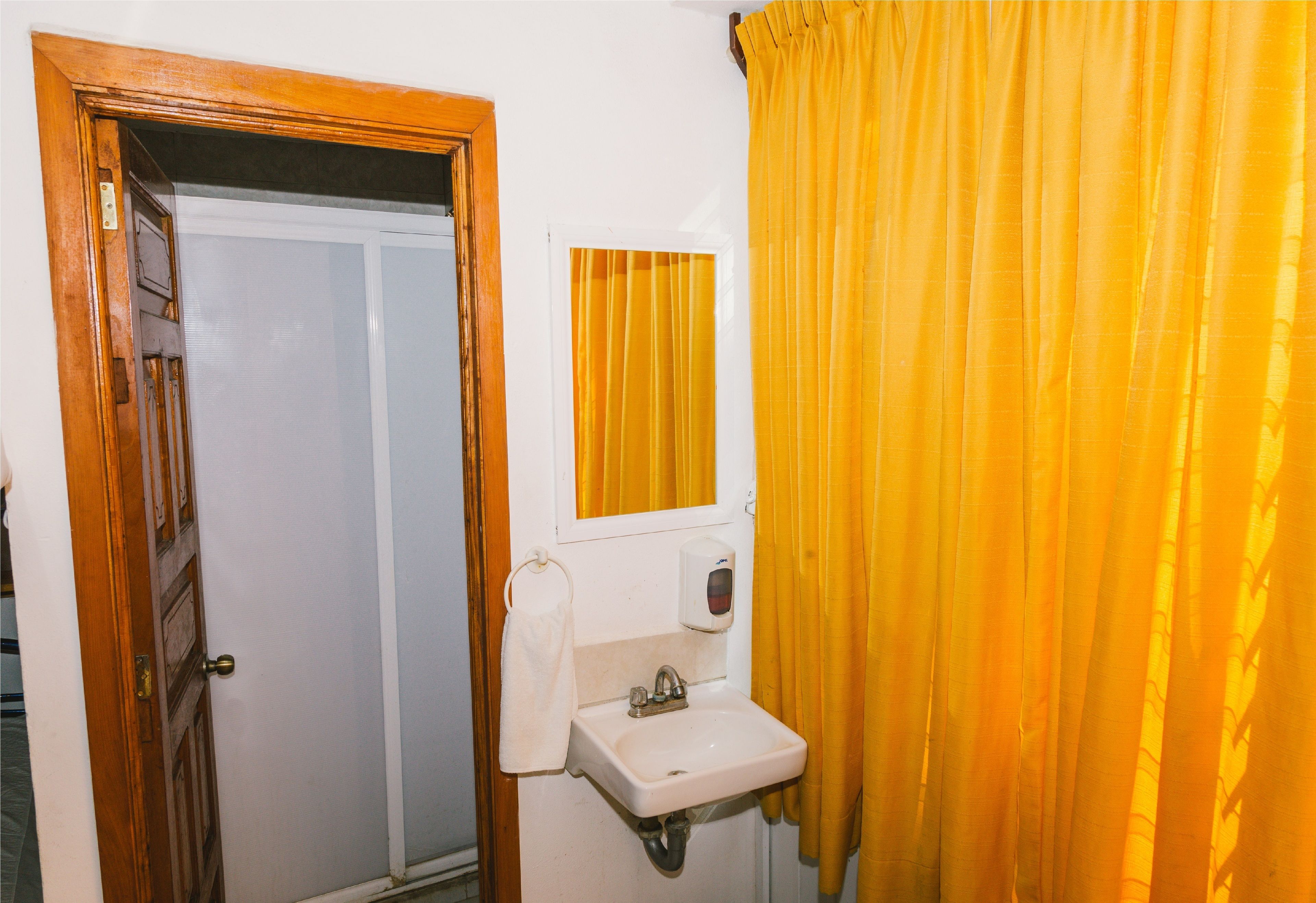 A bathroom with a wooden door, a white sink, a mirror, and yellow curtains.
