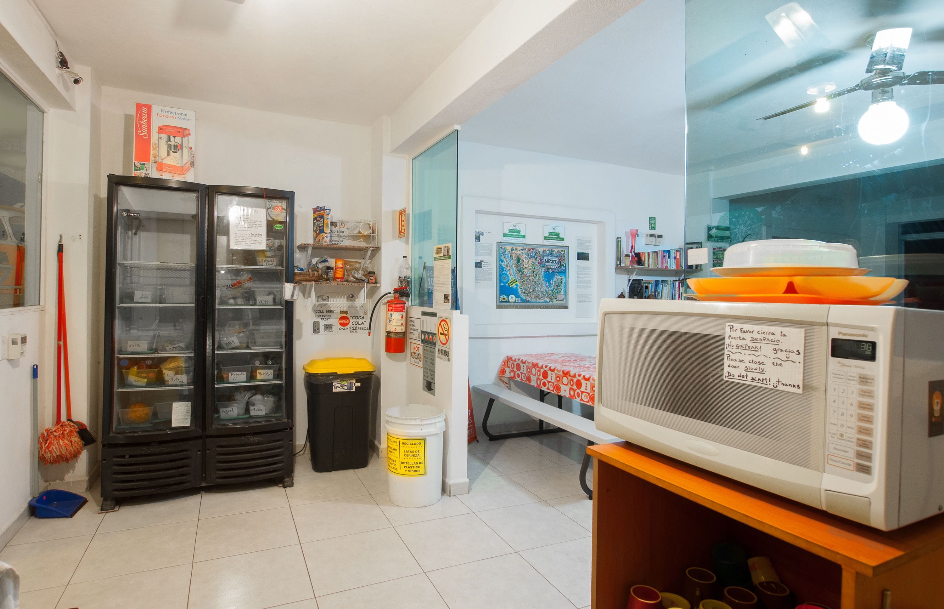 Una cocina equipada con refrigerador, microondas y lavadero. Se observan armarios, una escoba y un cubo.