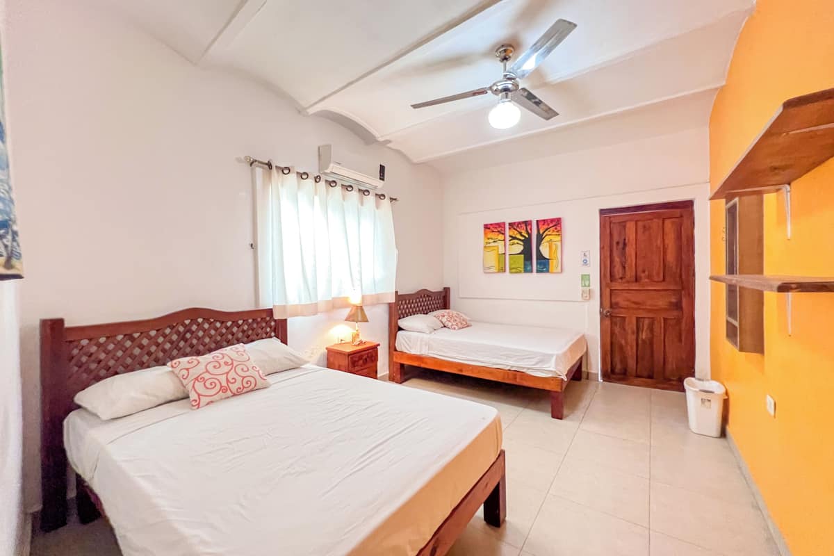 A room with two beds, a ceiling fan, and a window with curtains.