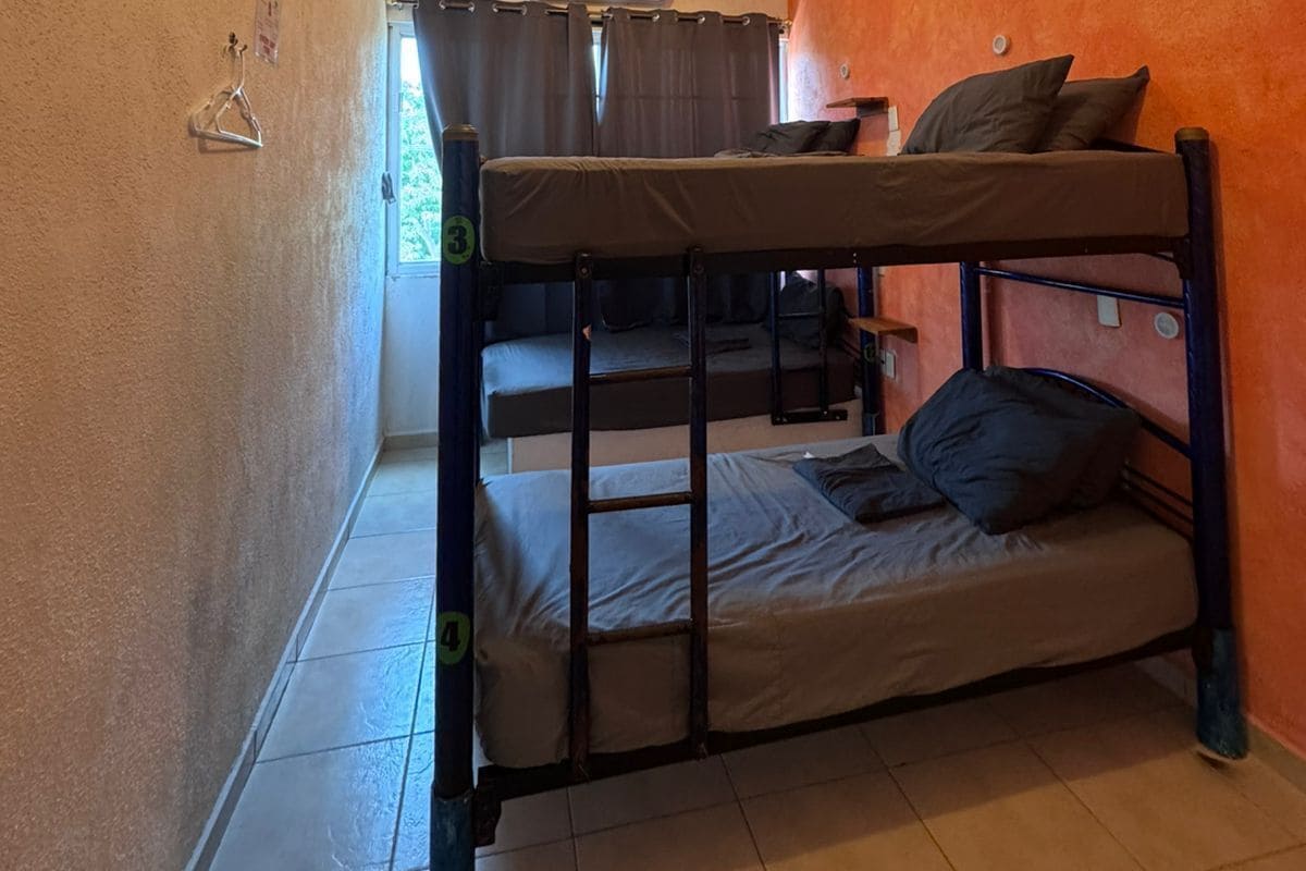 Een slaapzaal met stapelbedden, een kapstok, een airconditioning en een raam met gordijnen.