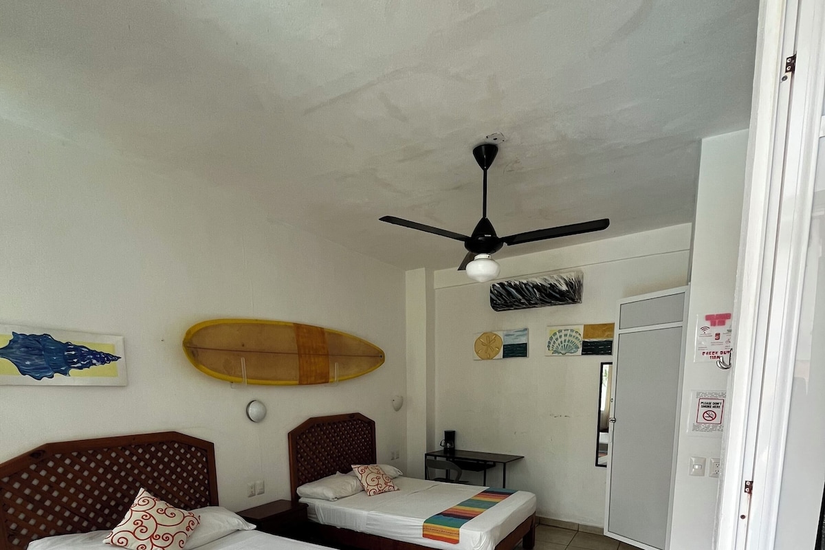 Een hotelkamer met twee bedden, een plafondventilator, een surfplank en een betegelde vloer.